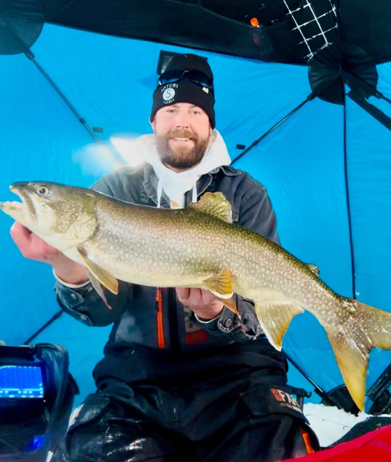 Angler holds chunky lake trout inside blue ice shack January 22, 2025 in Ely MN BWCA. Winter fishing report from Arrowhead Outdoors.