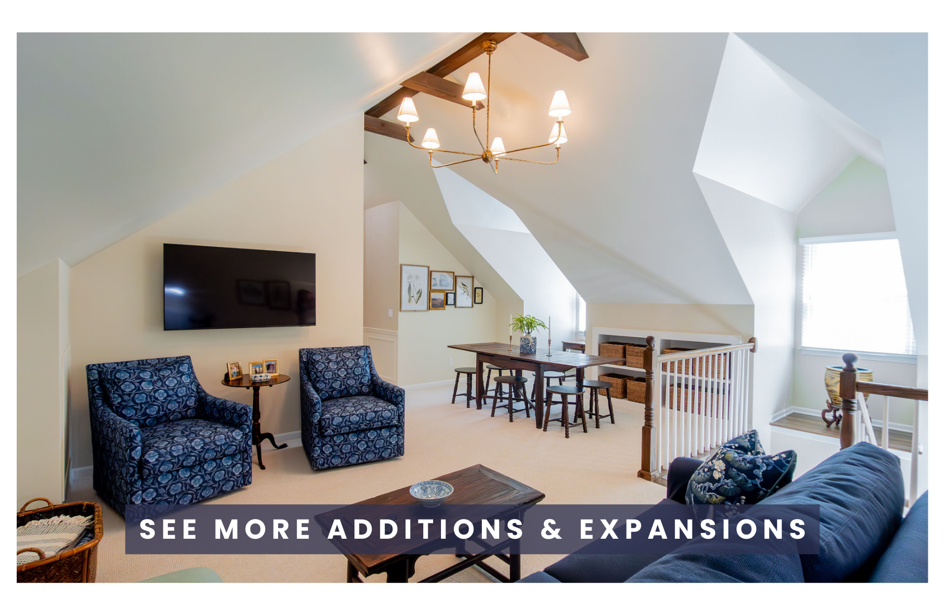 Attic loft with a patterned armchair, wooden table with a bowl, a couch with decorative pillows, a dining table with chairs and a plant, framed artwork on the wall, and a staircase railing.