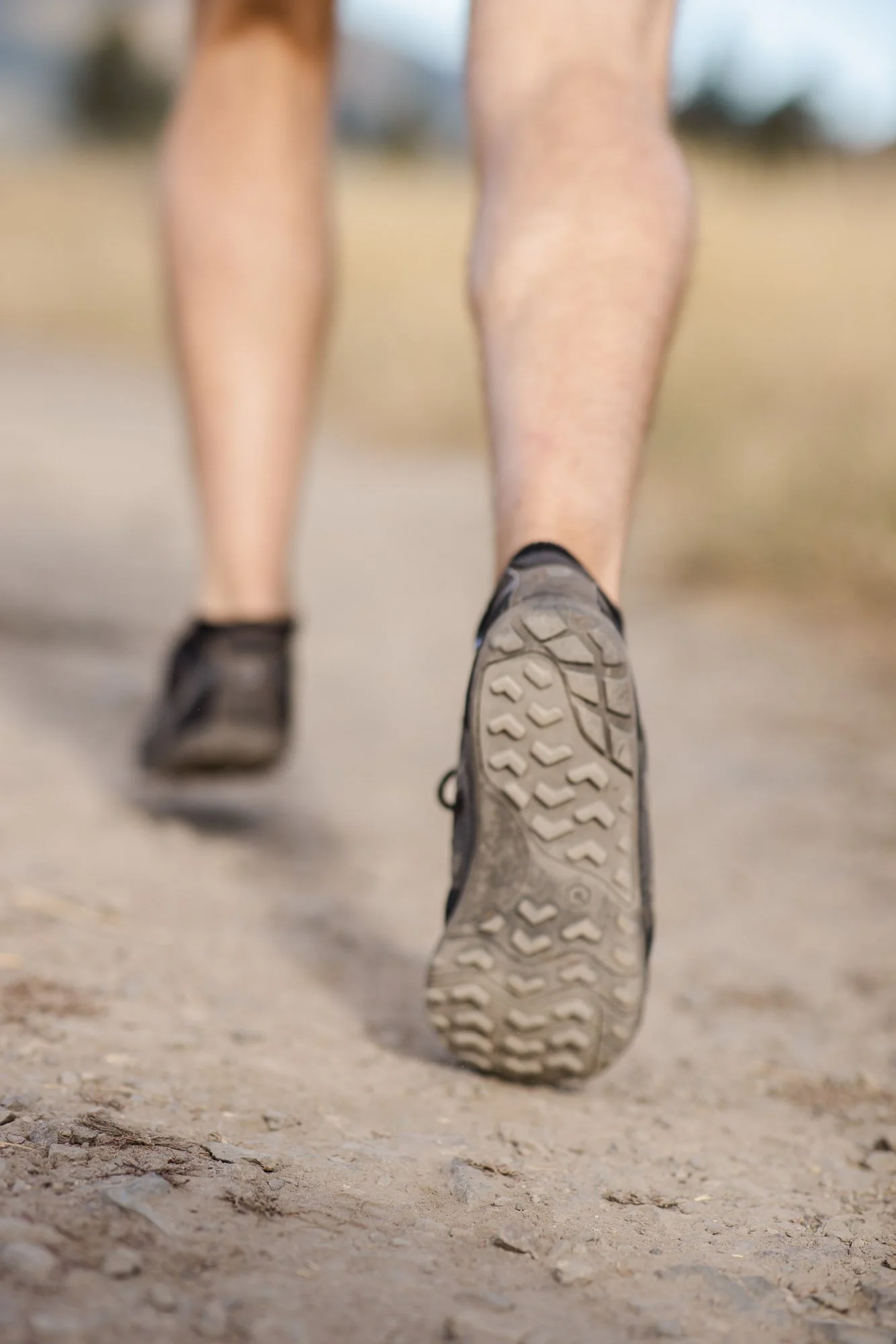Close-up of a person's legs and feet in hiking shoes walking on a dirt trail outdoors.