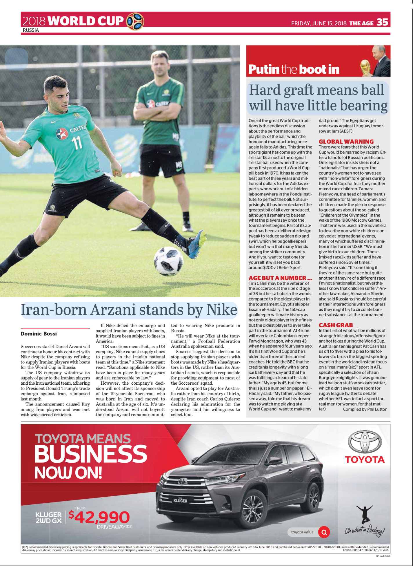 A soccer player in green uniform with black shorts is kicking a soccer ball on a field, with another player dressed similarly in the background.