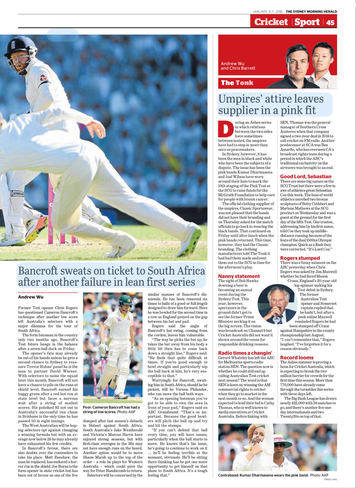 Cricket players in white uniforms on the field, one sliding to stop the ball, with a crowd in the background.