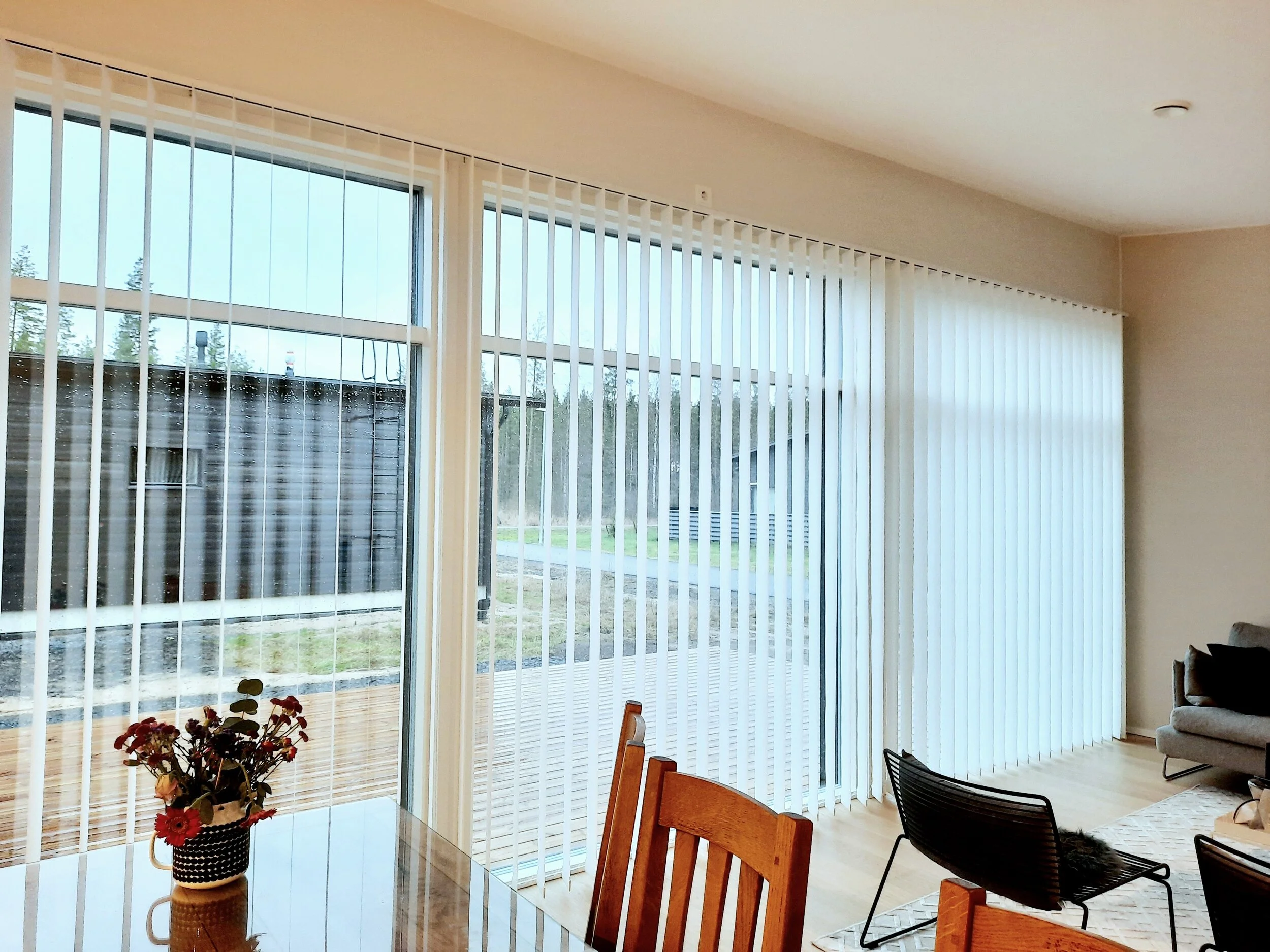 Moderni keittiö-olohuone, jossa ikkunoita koko seinän leveydeltä. Ikkunoiden edessä valkoiset, moottoroidut pystylamelli-verhot.