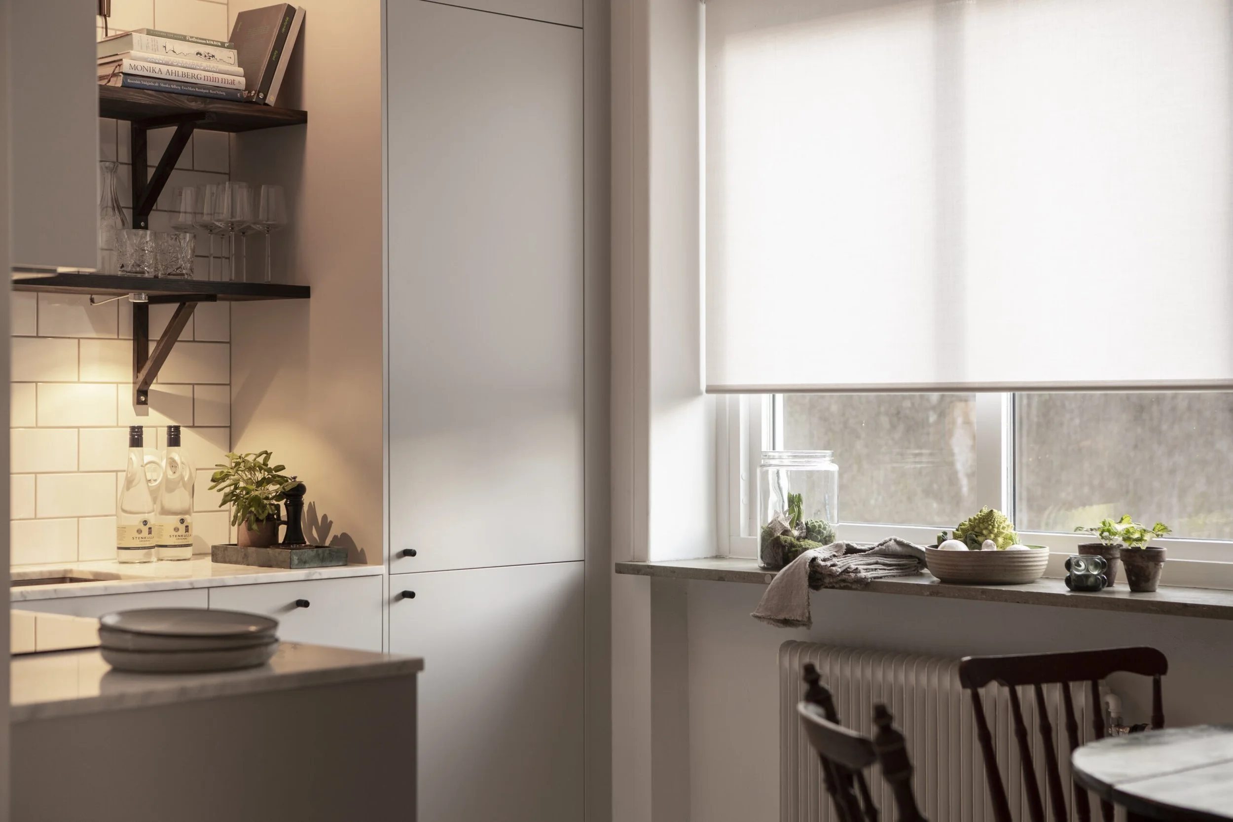 Moderni keittiö, jossa vaaleat kaapistot. Keittiössä on iso ikkuna, jonka edessä on valkoinen screen-rullaverho.