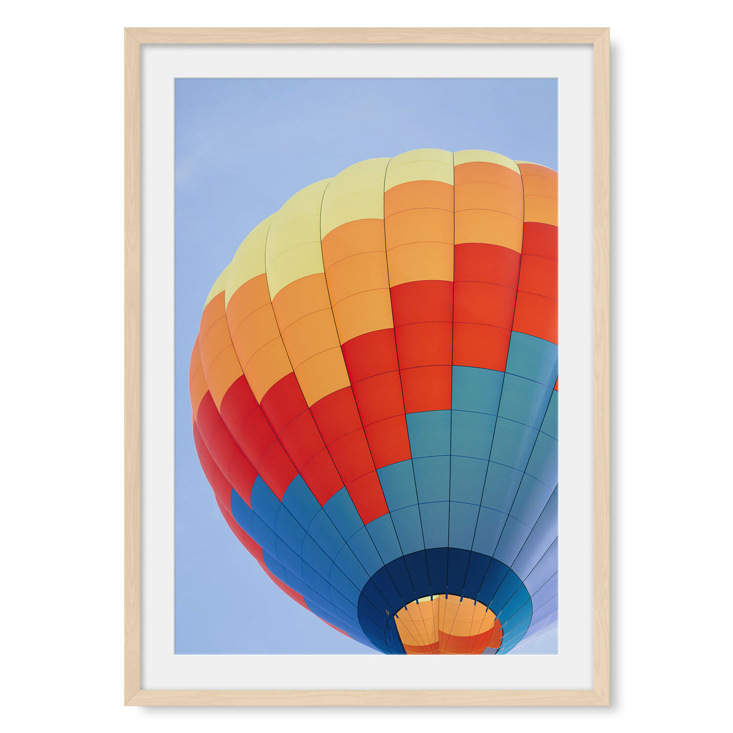 Light maple solid hardwood framed vertical fine art photography of a blue, red and orange hot air balloon preparing for takeoff against a clear blue sky.