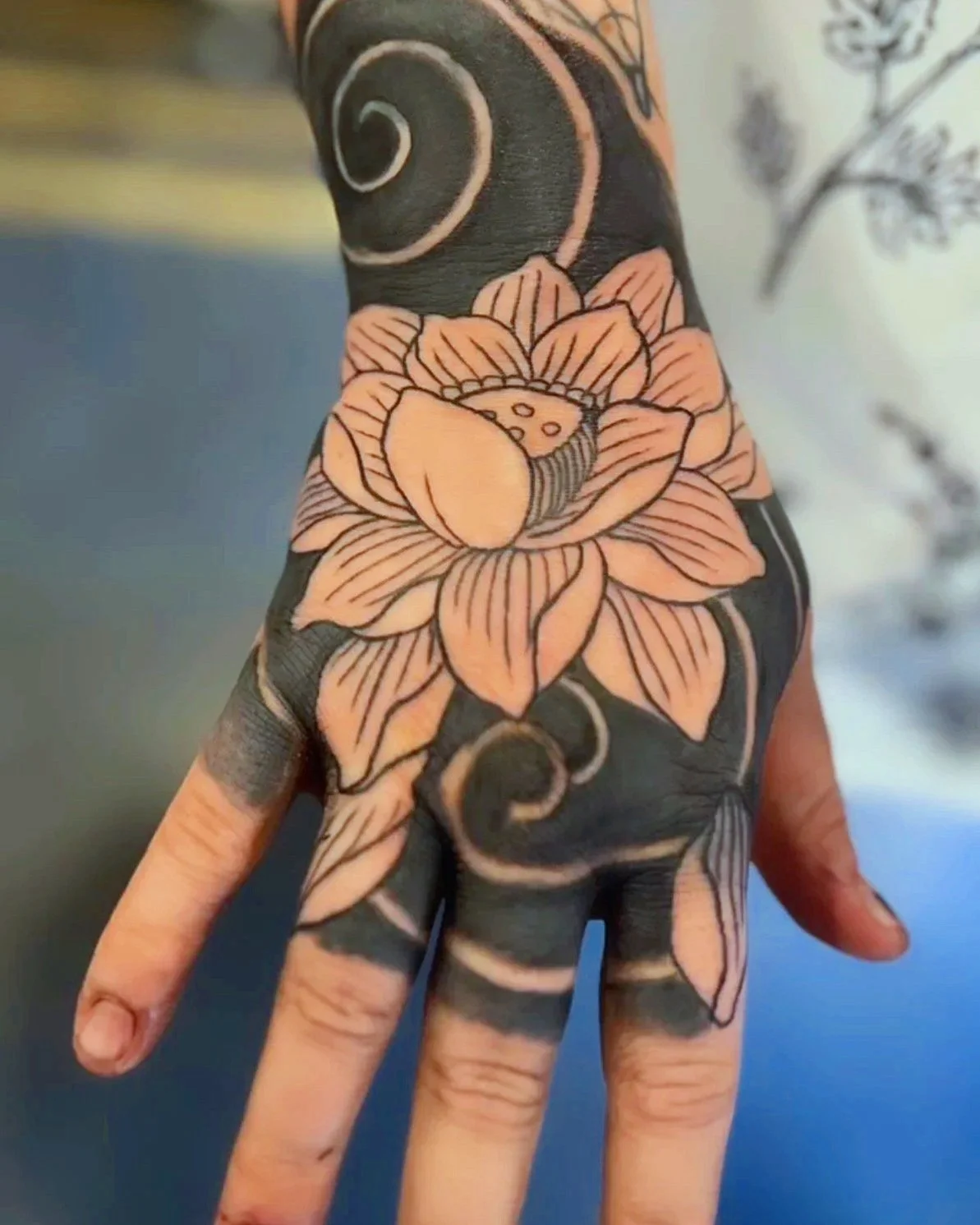 Tattoo of a flower on a person's hand and wrist, with black and light pink ink details.