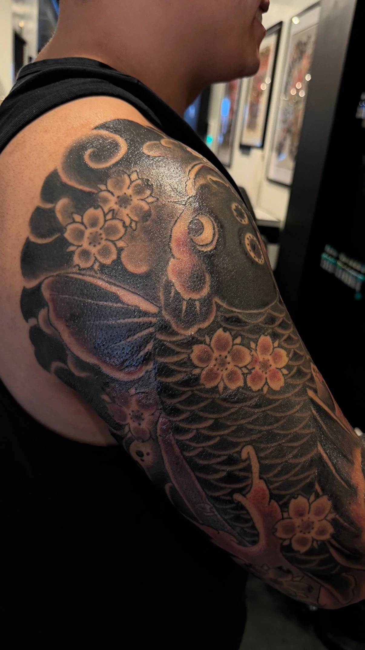 Colorful tattoos of cherry blossoms, a butterfly, a koi fish, and a lucky cat on a person's upper arm and shoulder.