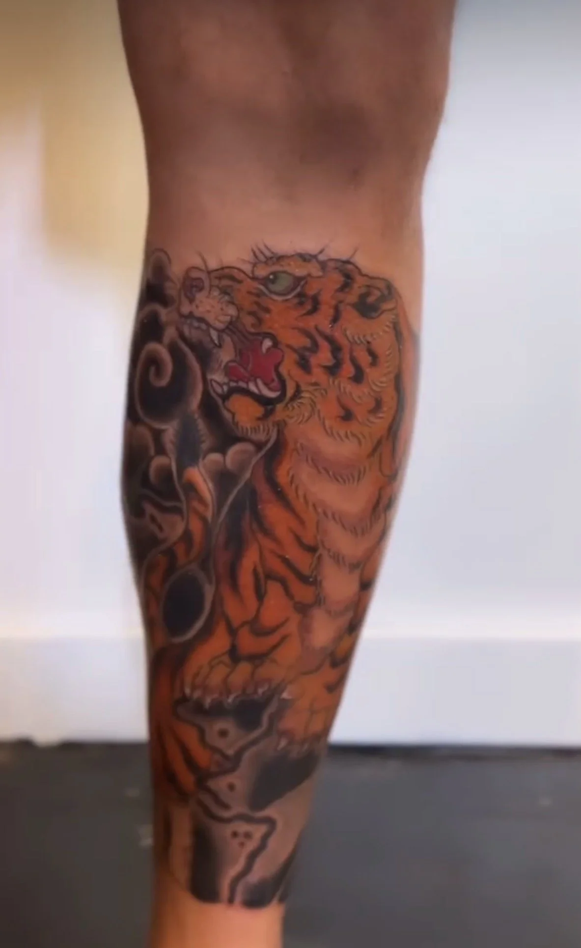 Tattoo of a tiger's head on the person's thigh, with surrounding designs in black and orange ink.