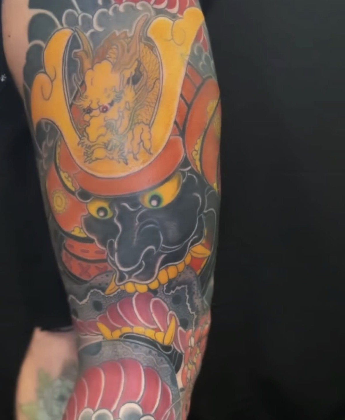 Tattoo sleeve featuring a fierce tiger head, a black oni mask, colorful flowers, and traditional Japanese elements in bold colors.