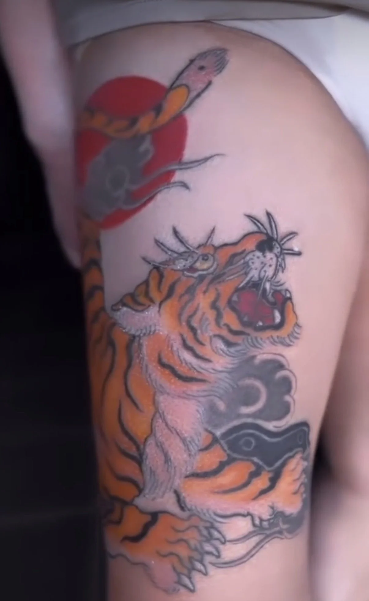Tattoo of a tiger with its mouth open on a person's upper arm, with a smaller dragon tattoo above it.