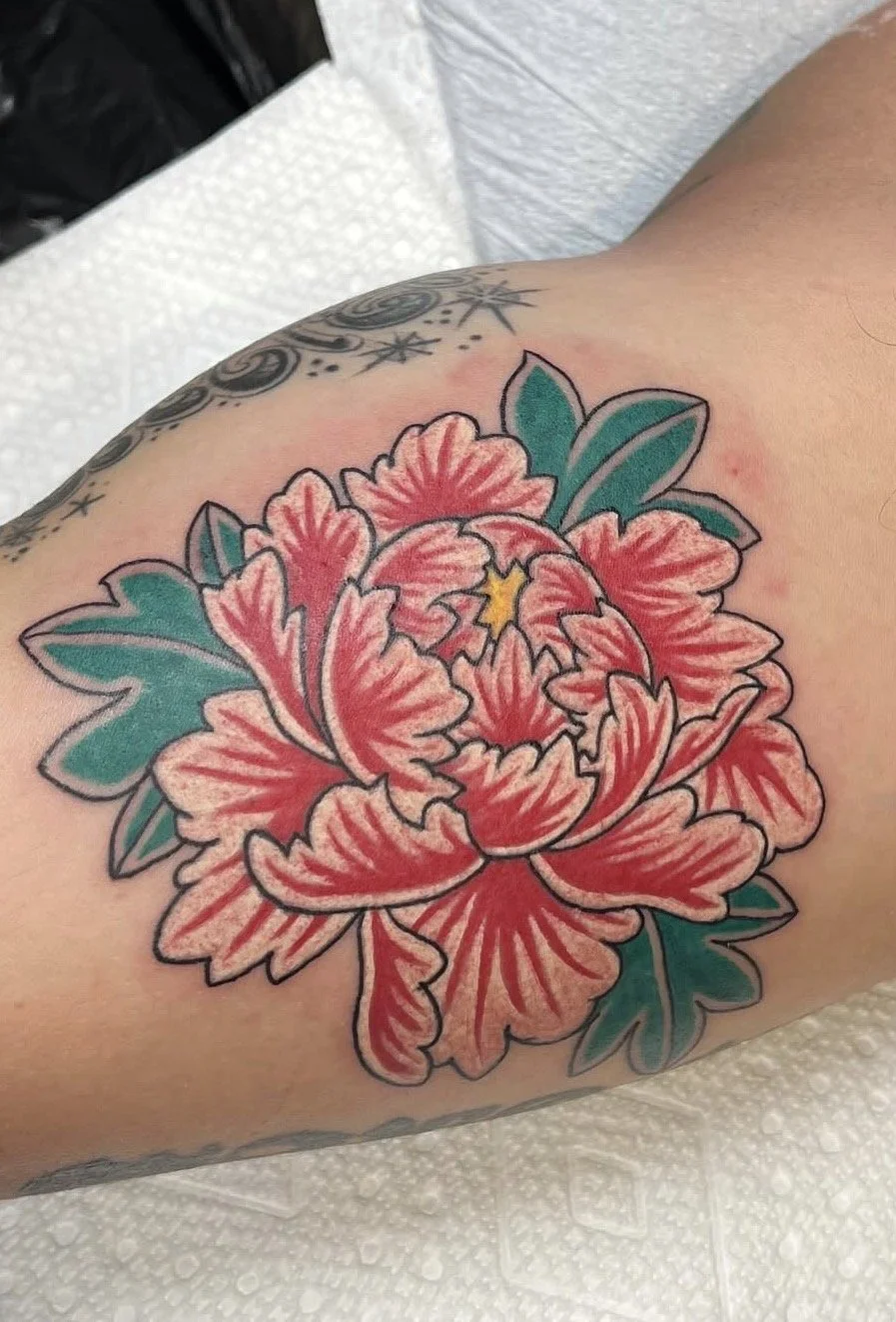 Colorful tattoo of a pink flower with green leaves on a person's arm.
