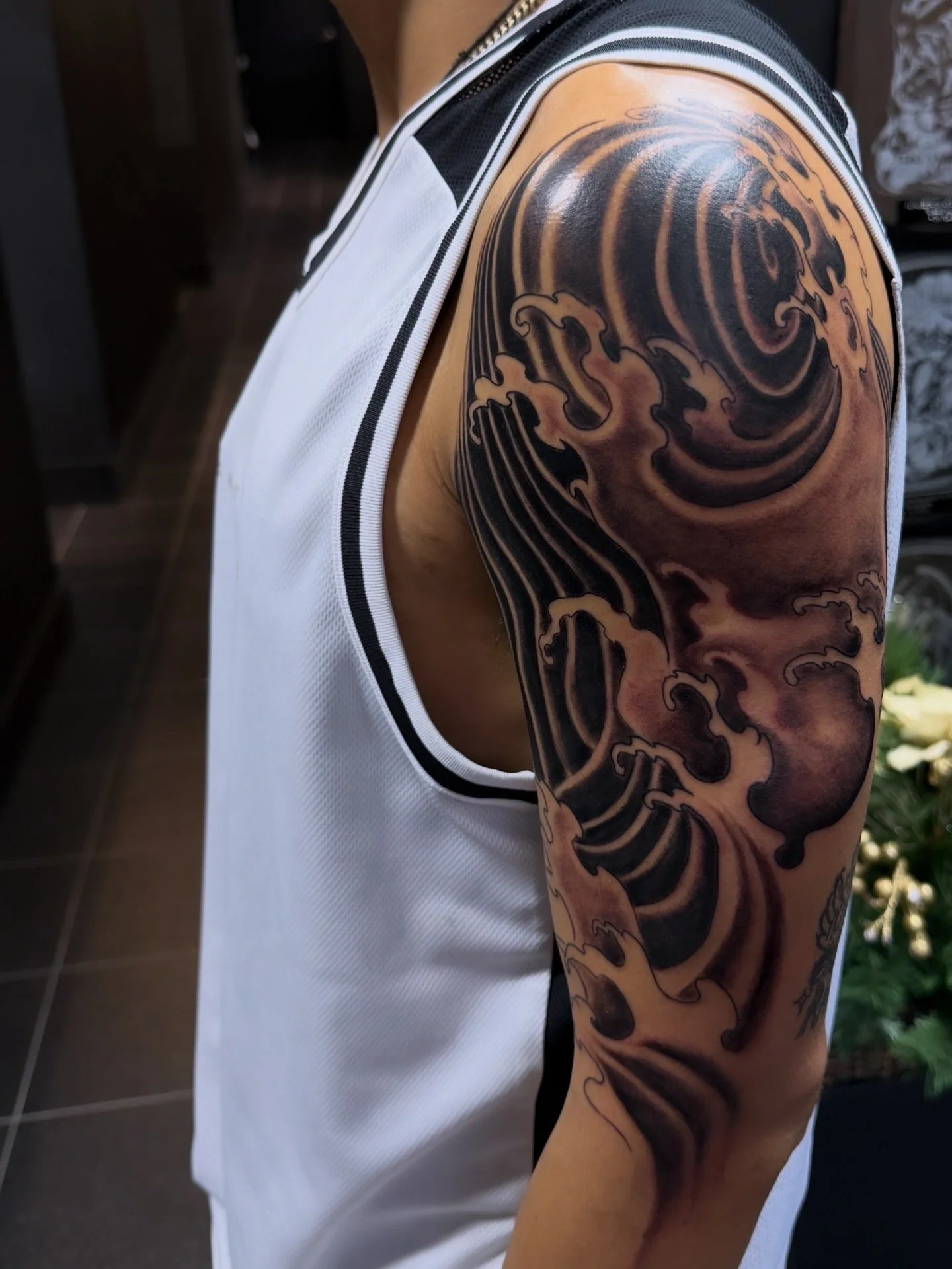 Tattoo of a large wave on person's upper arm and shoulder.