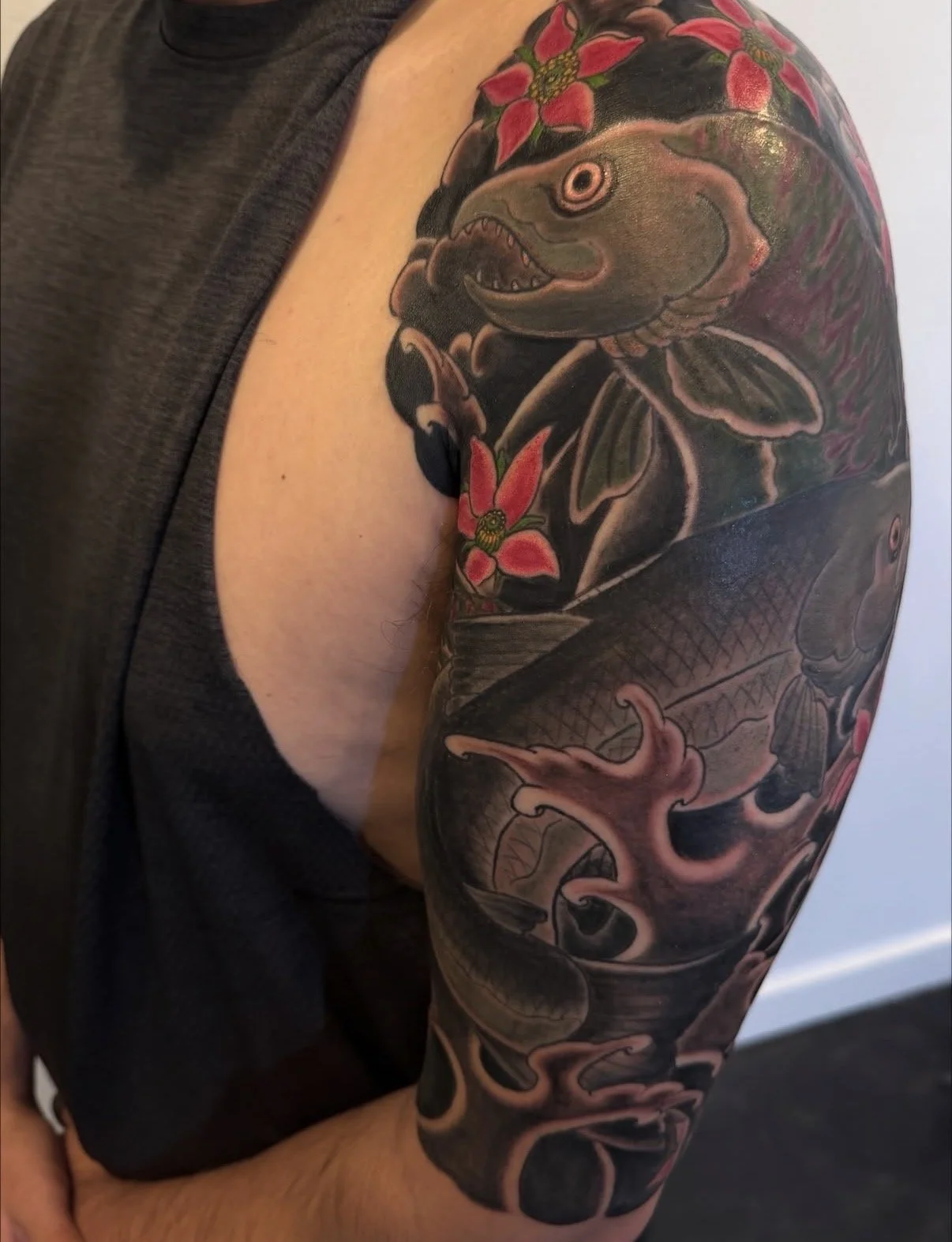 A tattoo sleeve featuring a fish, flowers, and a prehistoric creature.