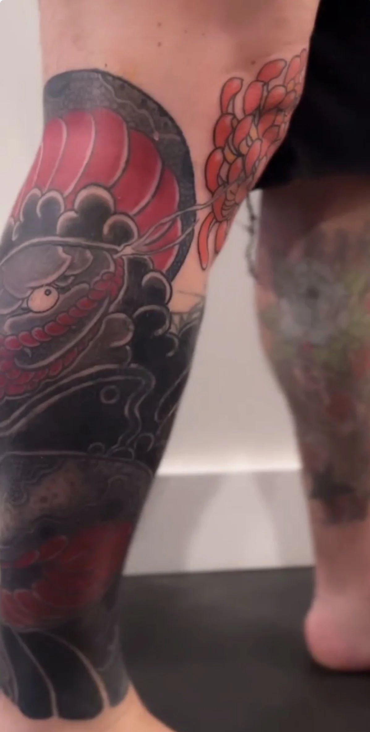 Close-up of a leg with Japanese-style tattoo artwork featuring a koi fish and floral patterns.