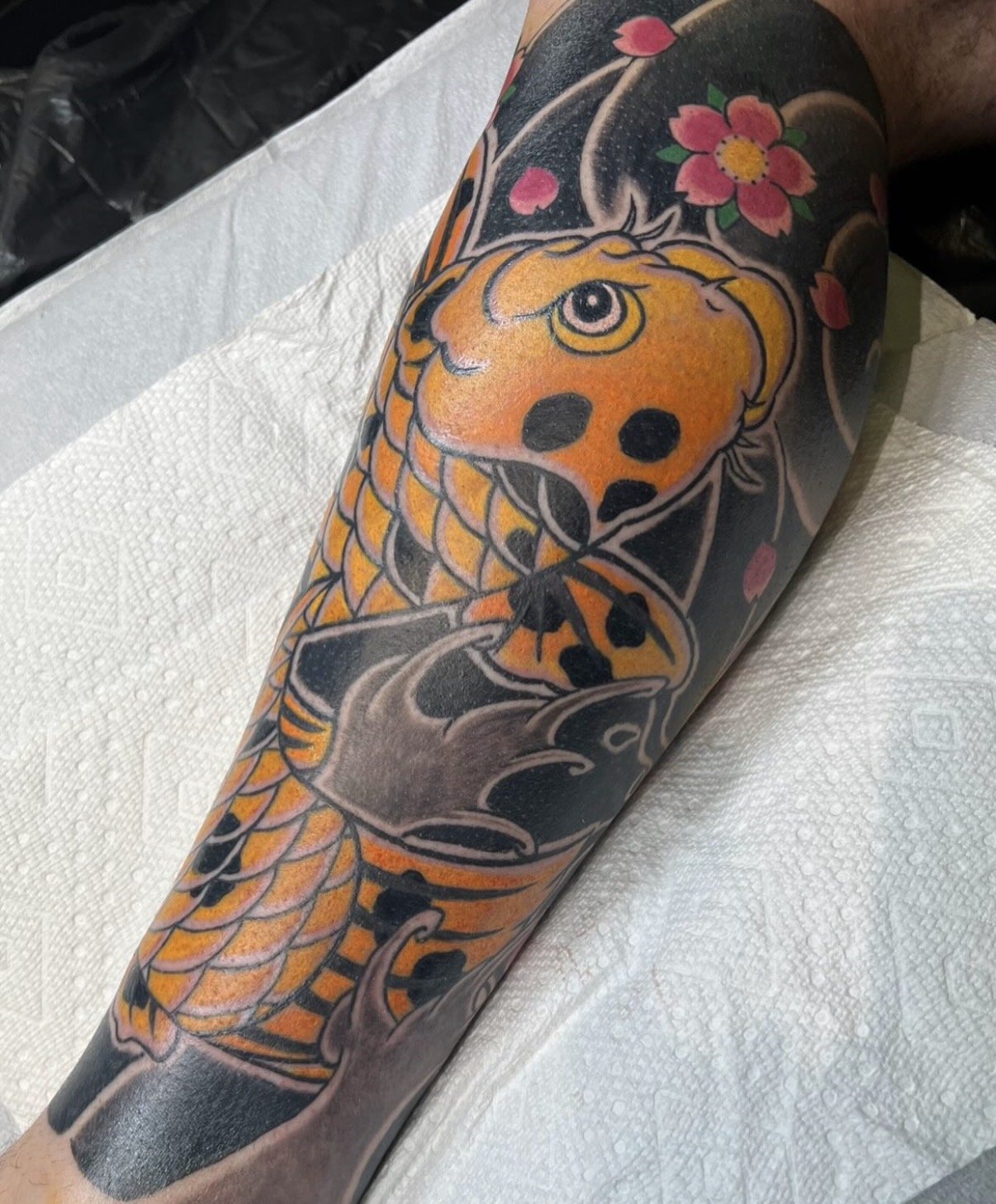 Colorful tattoo of a dragon and a skull with cherry blossoms on a person's arm.