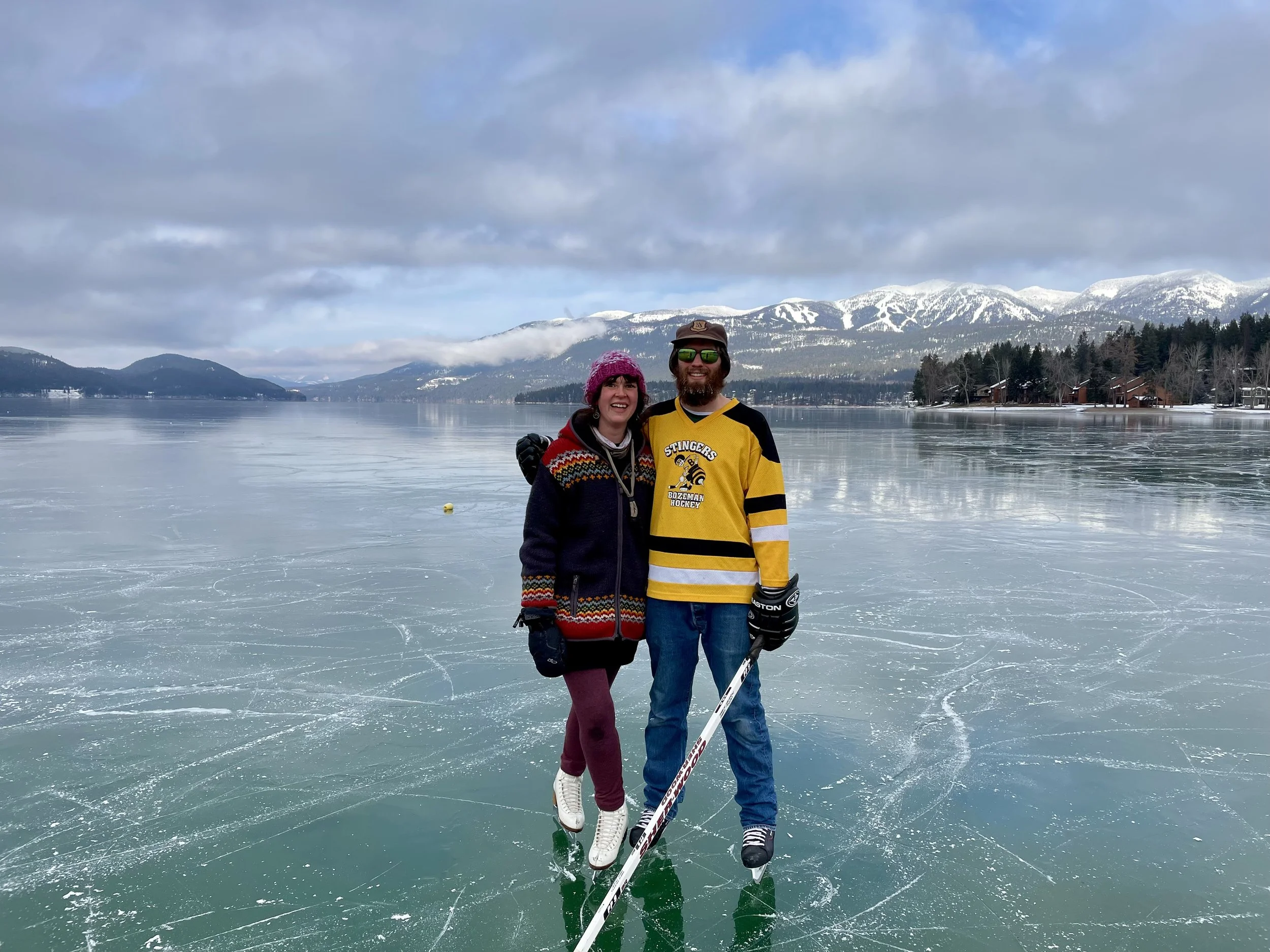 Creative Combinations Montana's owners Nate Stoltzfus and Kelsey Holmes ice skating on black ice on Whitefish Lake, in Whitefish Montana, with Big Mountain in the background.