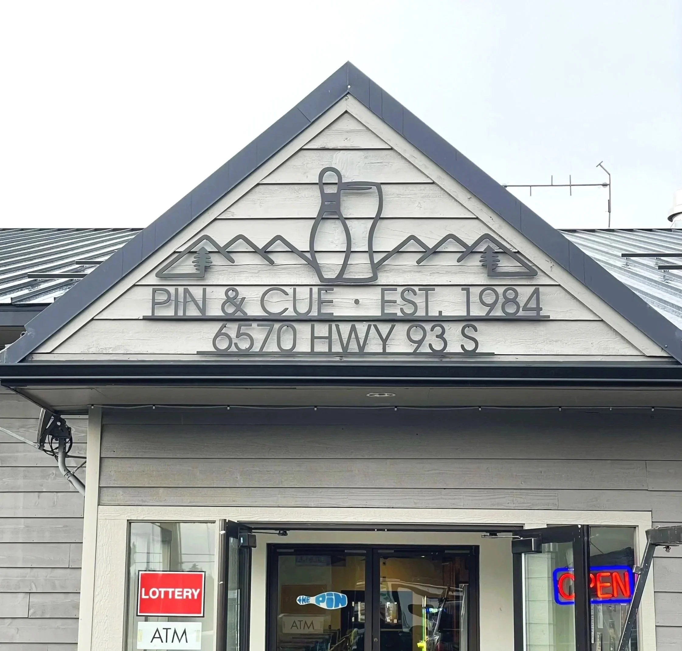 Custom steel business sign for Whitefish Montana based  'Pin & Cue, Est. 1984, 6570 HWY 93 S,' featuring mountain and pine tree graphics fabricated and installed by Creative Combinations Montana.