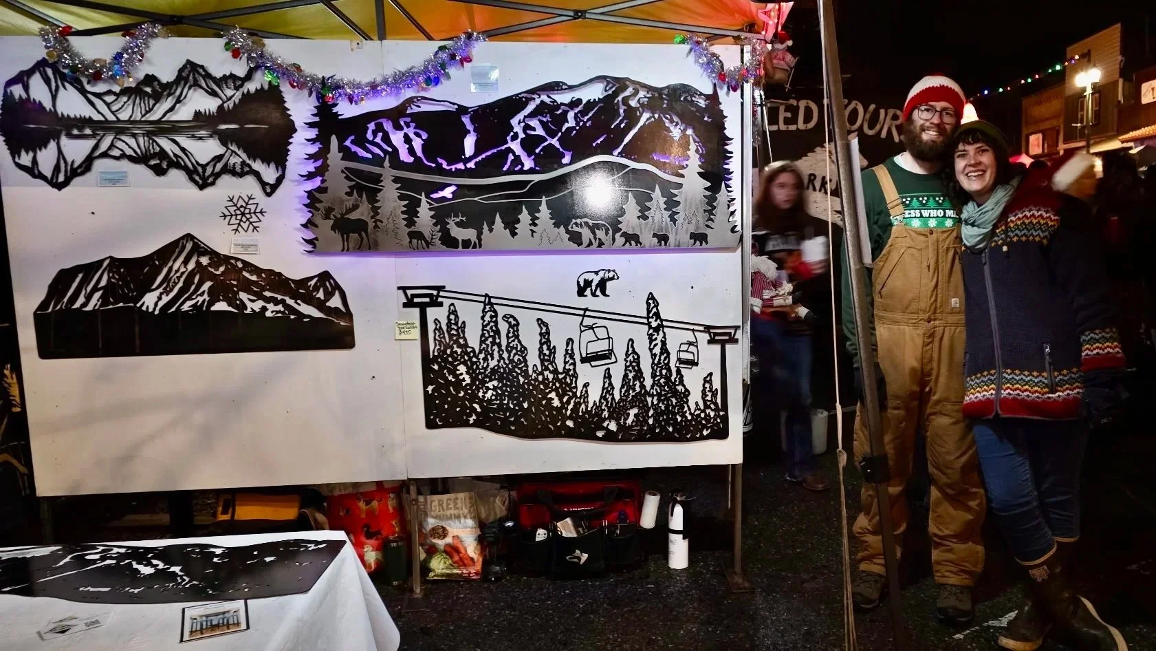 Photo of Creative Combinations Montana's owners Nate Stoltzfus and Kelsey Holmes at the Whitefish Christmas Stroll with their Big Mountain Metal wall art LED piece.