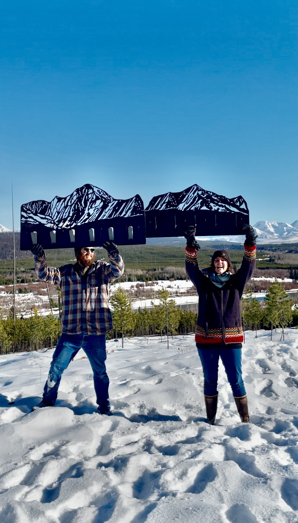 CCMT's owners Nate Stoltzfus and Kelsey Holmes holding custom steel mountain coat racks in front of the the mountains they are designed from in Glacier National Park Montana.