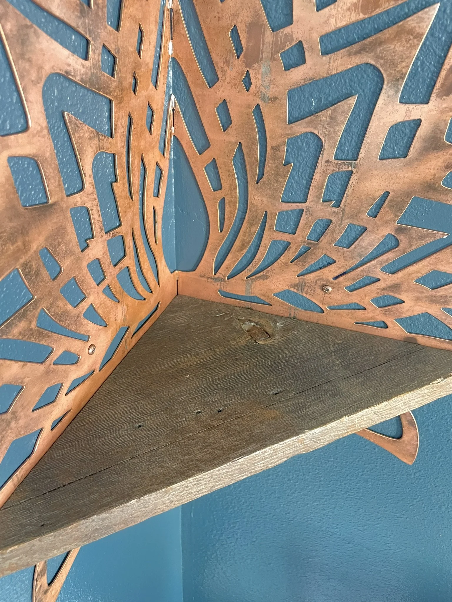 Close up photo of Creative Combinations Montana's Thousand Petal Lotus Steel and Wood Corner Shelf,  finished with a copper patina finish and barnwood shelf.