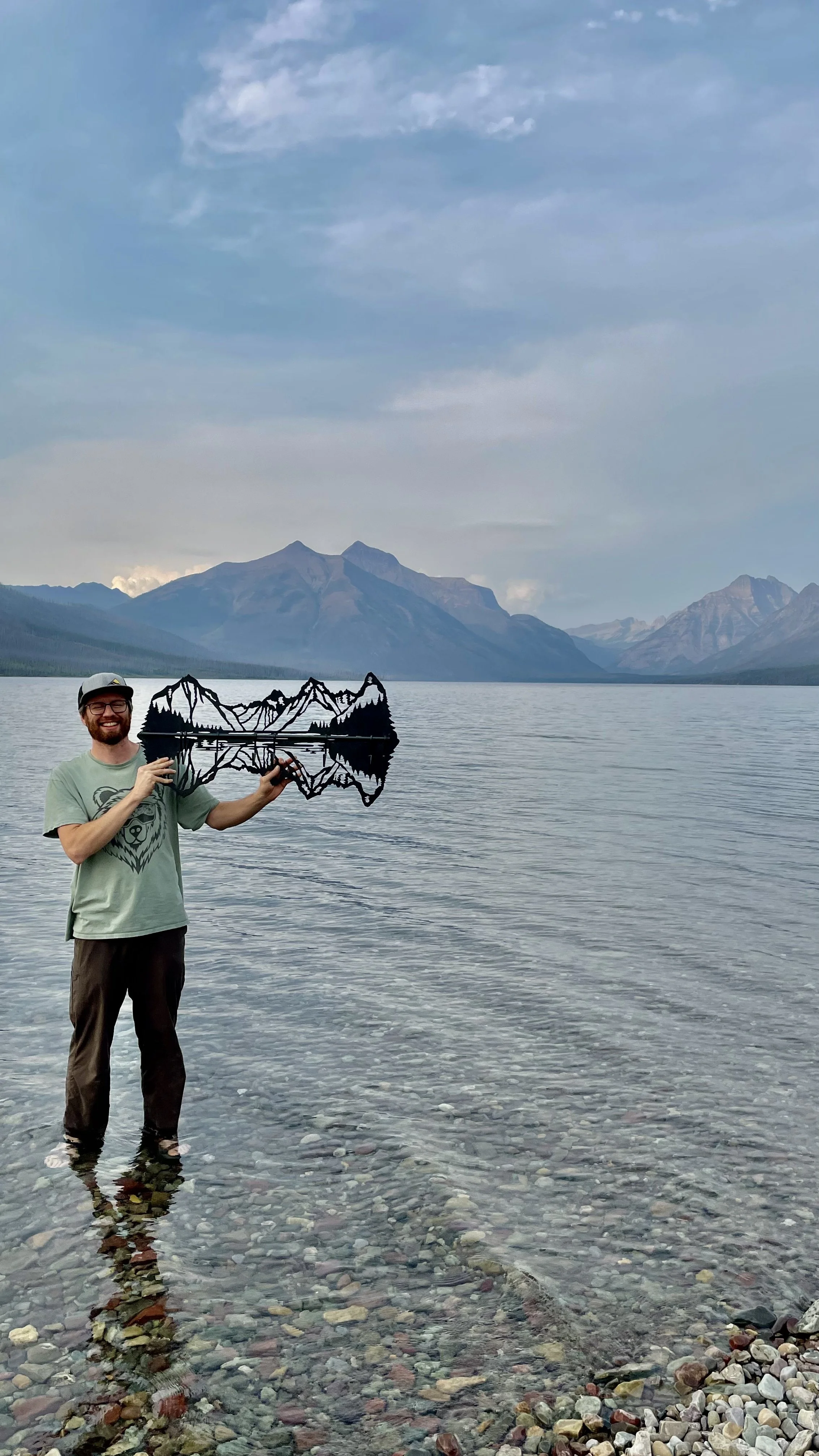 CCMT's owner Nate Stoltzfus holding a Lake McDonald Metal Wall Art at Lake McDonald in Glacier National Park in Montana.