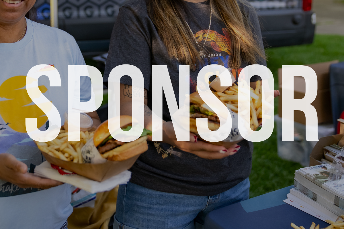 Two people holding half a hamburger with fries at an outdoor event table.