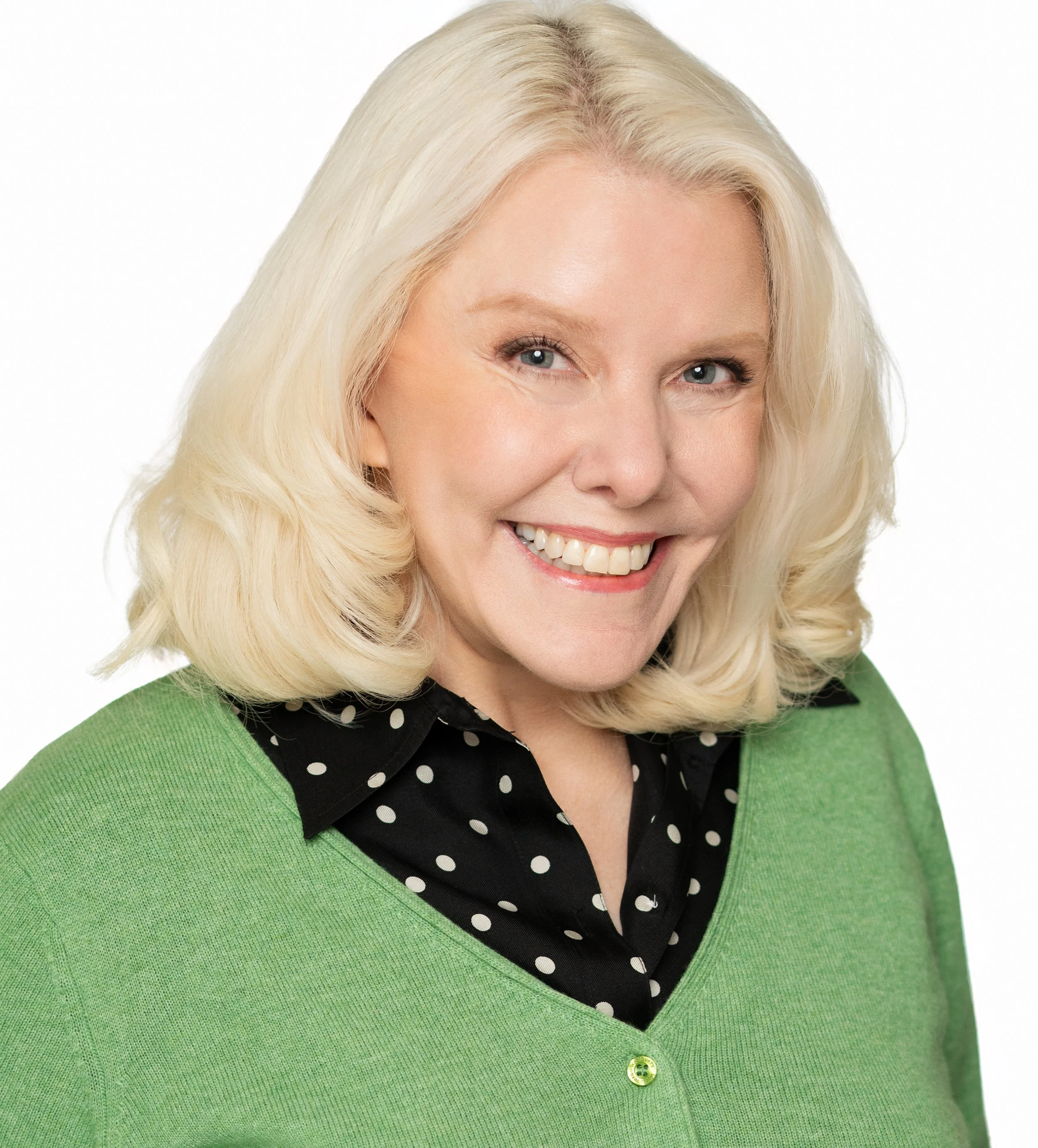  Atlanta headshot of a smiling woman with blonde hair, wearing a green cardigan over a black blouse with white polka dots, against a white background.