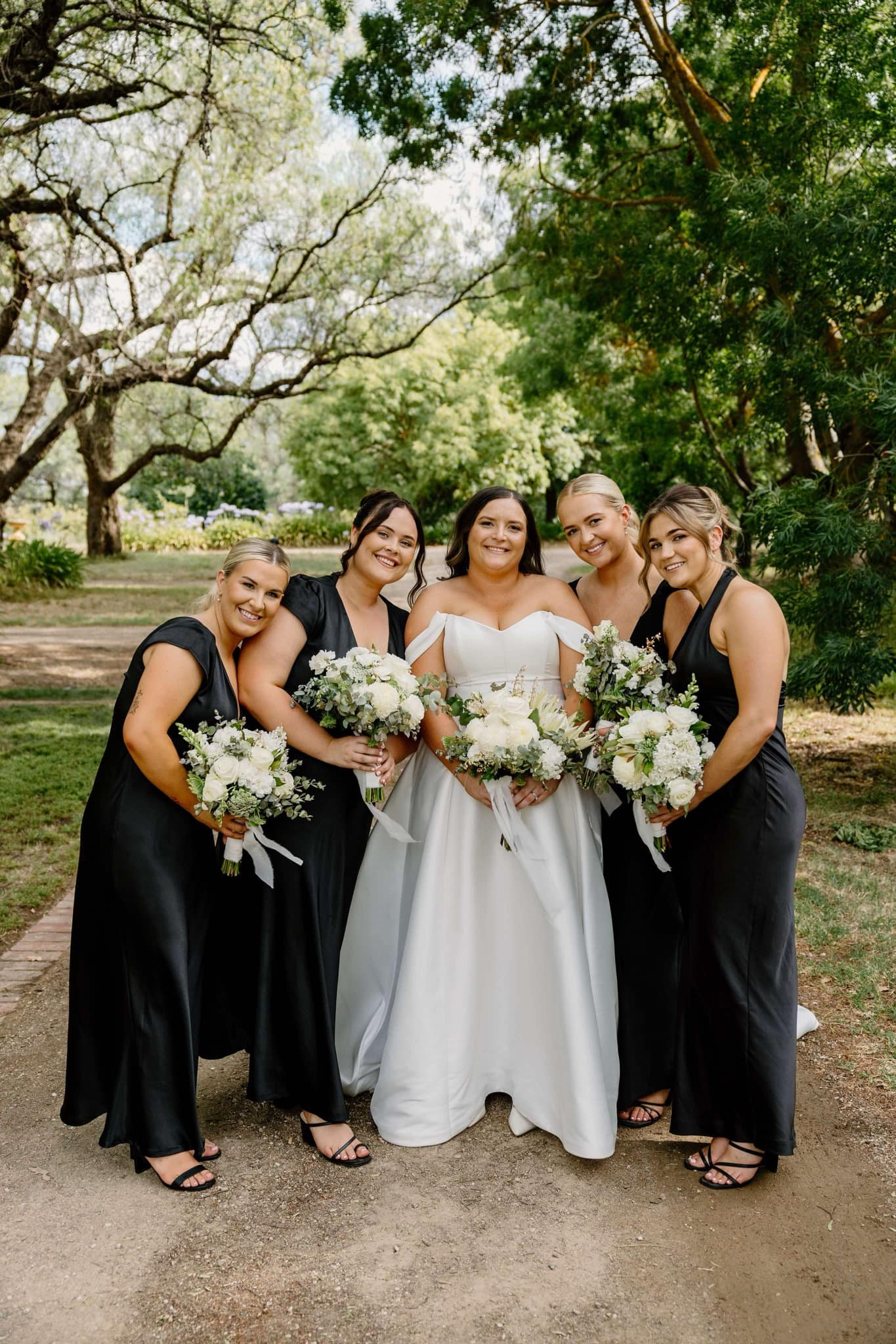 Bride and bridesmaids in dresses holding bouquets in a garden setting.