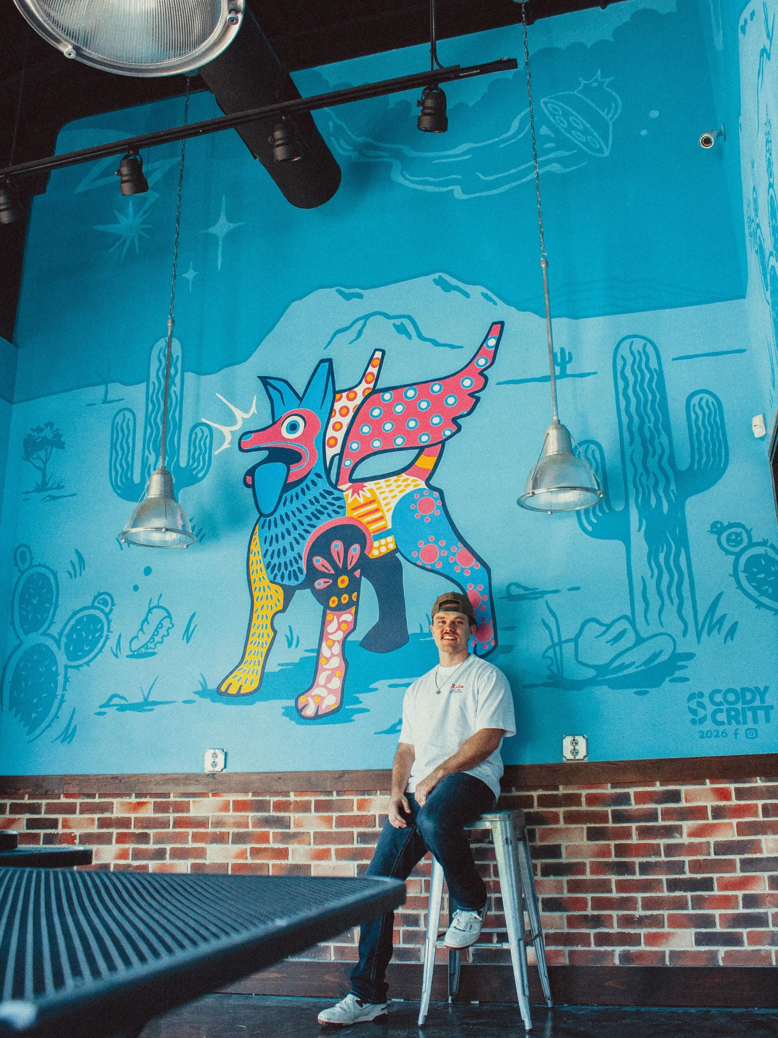 ITS BEEN A MINUTE!! This is my latest mural I painted at the upcoming TACO TACO in Columbia, MO!! We&rsquo;ve been working on the style of this mural for months and eventually landed on this bold blue desert background that matches the logo for TACO 