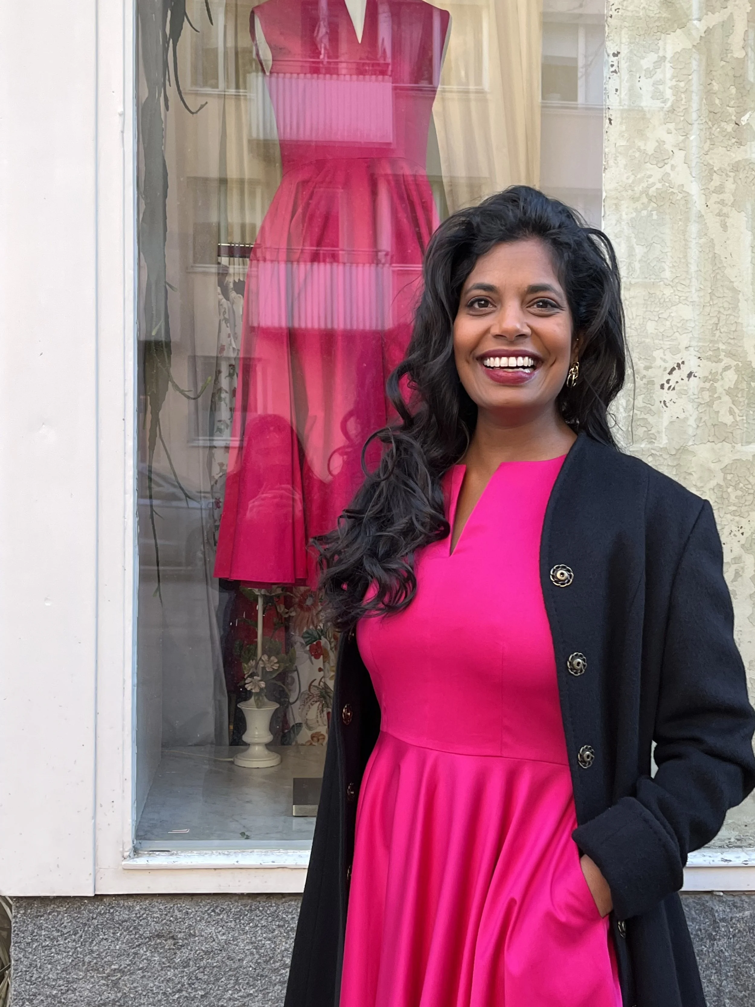 Kvinna i rosa klänning utanför en butik med en rosa klänning i fönstret.