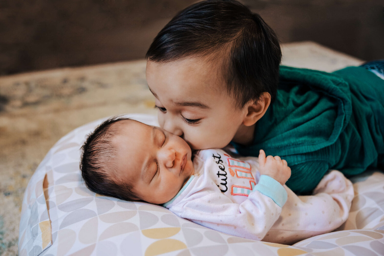 Lifestyle toddler brother kissing newborn baby girl