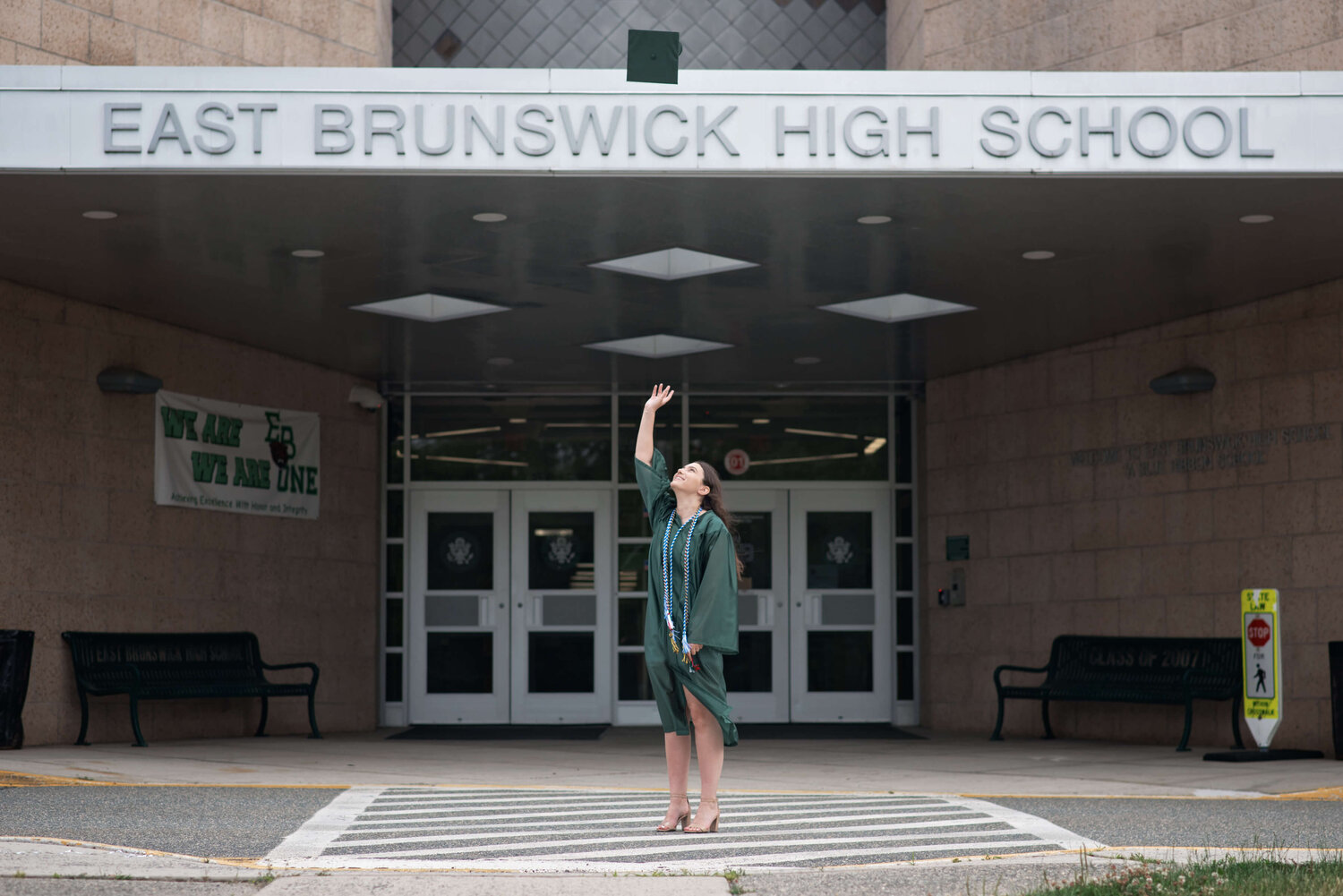 EBHS Senior Girl throwing graduation cap in front of high school