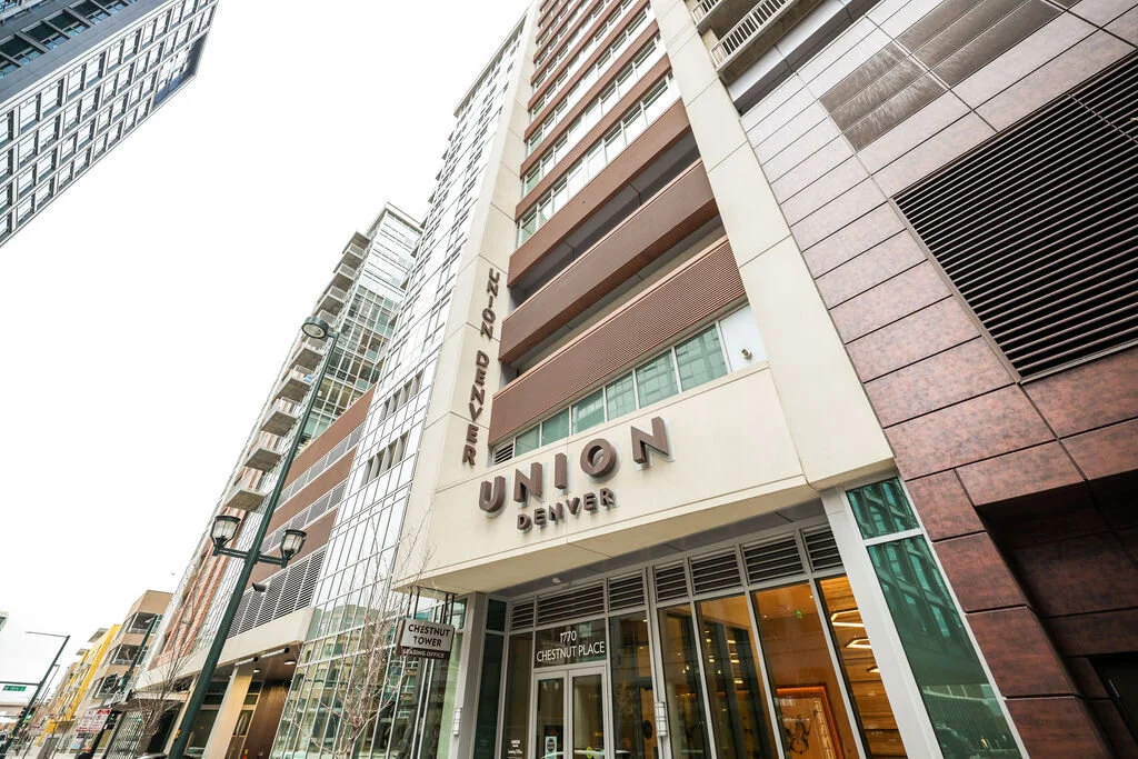 A lower angle image looking up at the Union Denver building exterior. This is a multistory building with reddish brown horizontal dividers between the floors and tan structural elements
