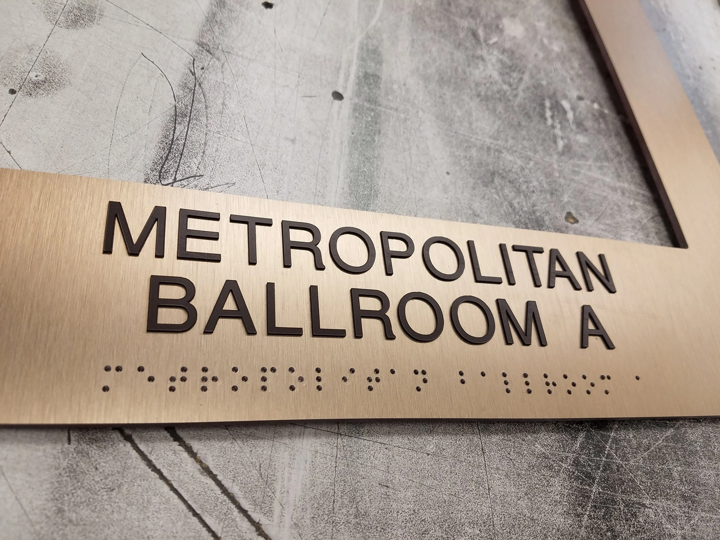 A brushed bronze face cover reading "Metropolitan Ballroom A" in dark brown tactile copy and Braille