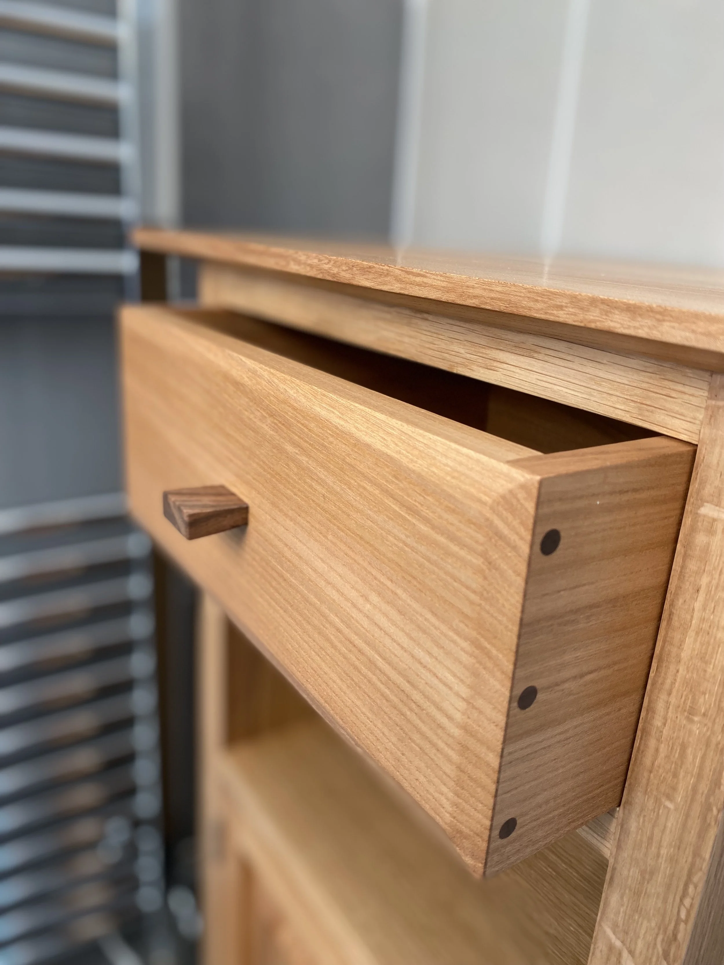 Close-up of a wooden drawer slightly open, part of a cabinet or furniture piece, with other similar drawers or furniture in the background.