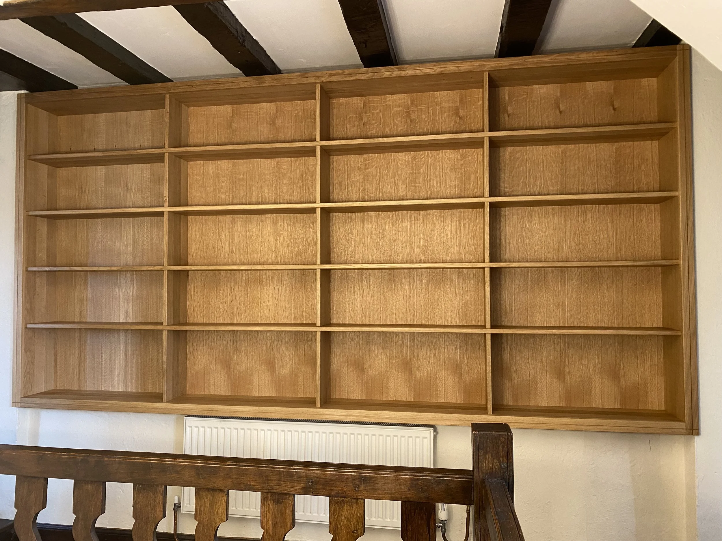 Empty wooden bookshelf with multiple compartments, situated against a wall with a radiator below.