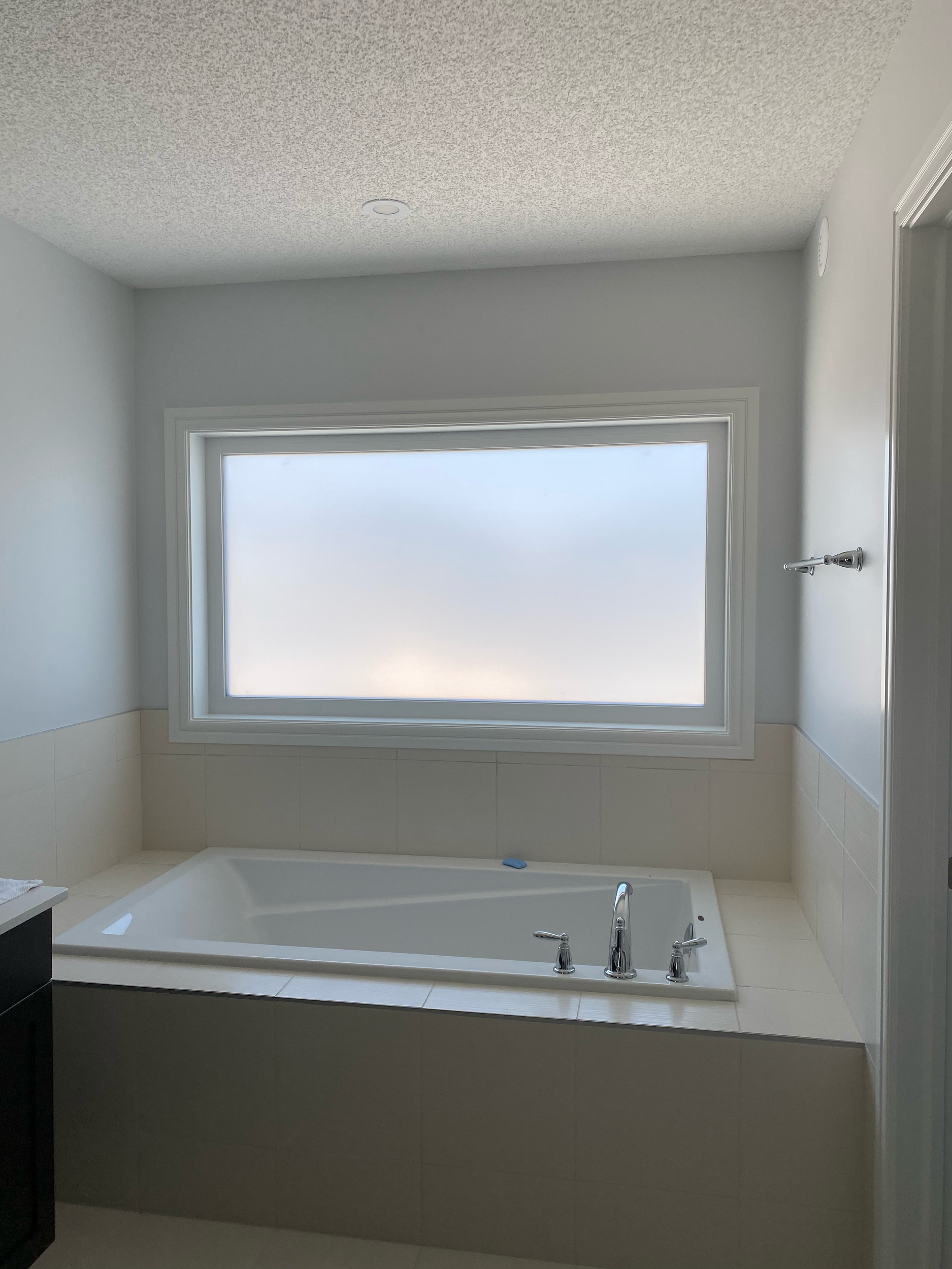 An unfinished bathroom with a window overlooking the sky, a bathtub, faucet, and tiled walls.