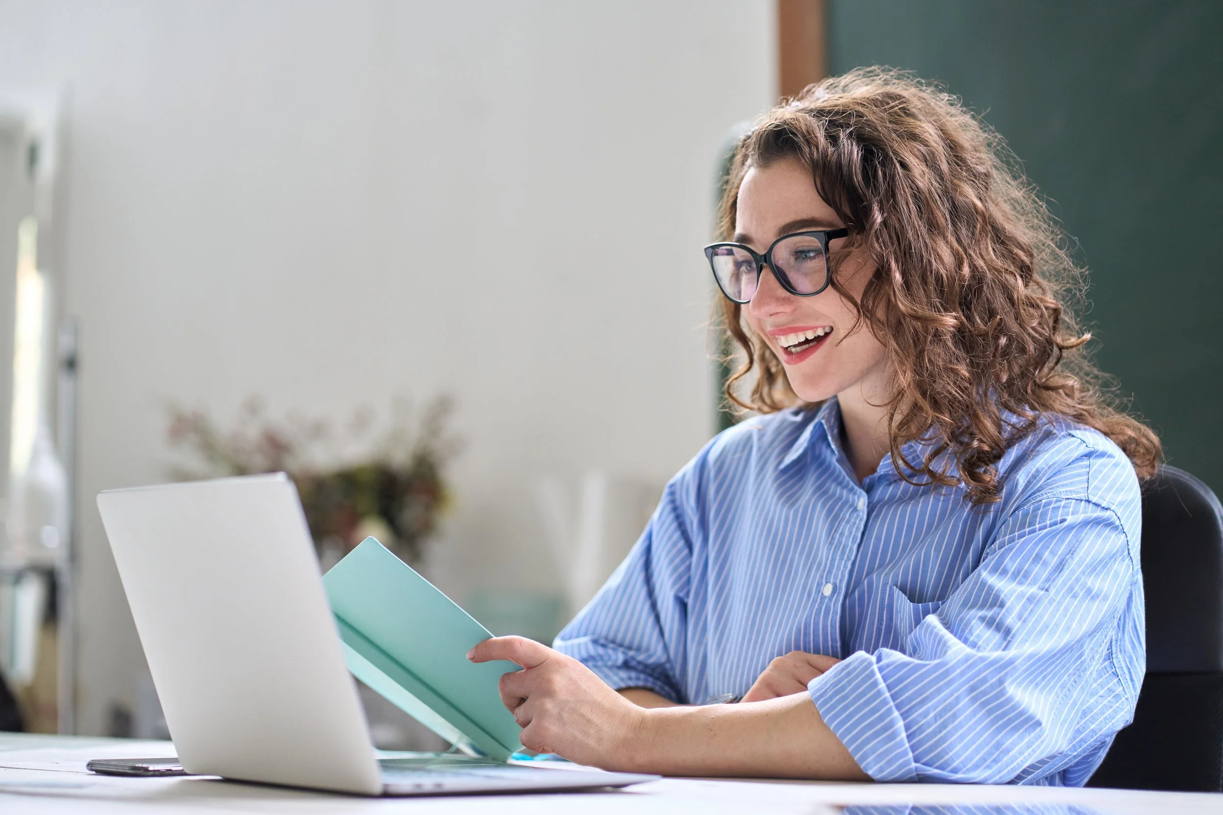 A Professional Virtual Assistant smiling while looking at a book in front of a laptop.