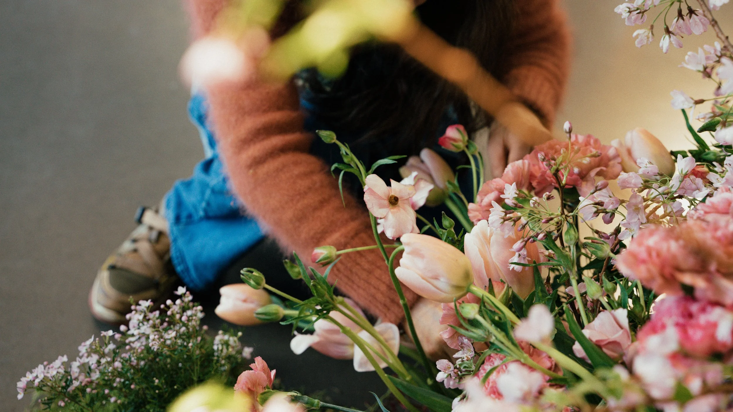Child arranging pink and white flowers amidst greenery on a dark surface.
