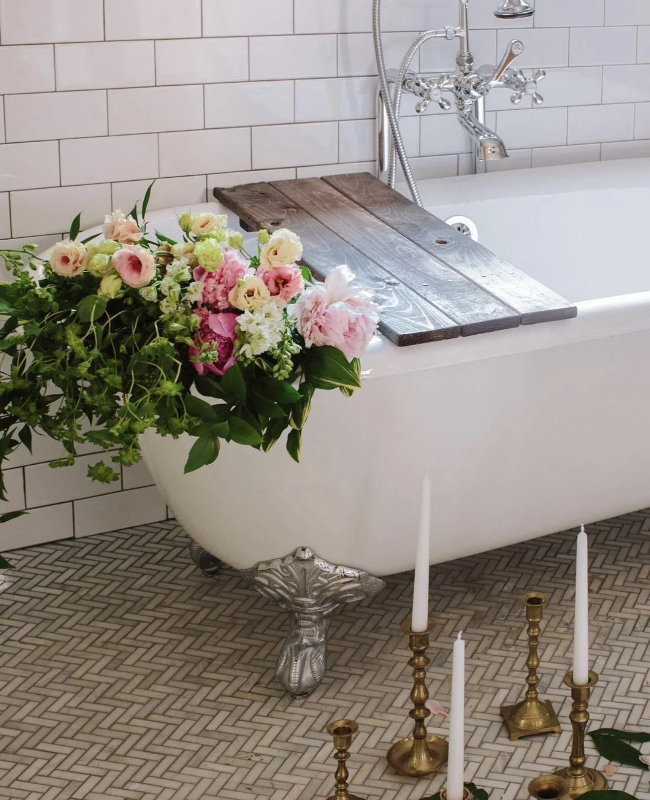 Pink and cream peonies arranged beside a vintage clawfoot bathtub in a bright bathroom.