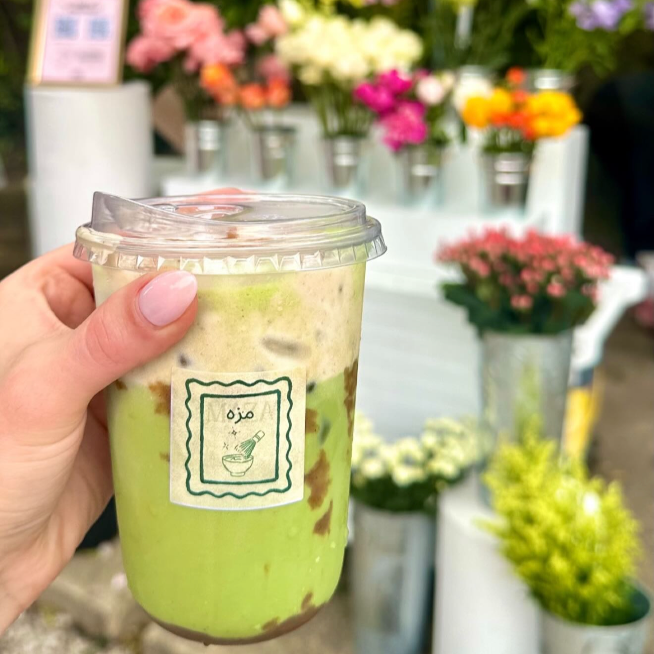 Iced matcha held in front of fresh flower displays at Rudy's Flower Truck.