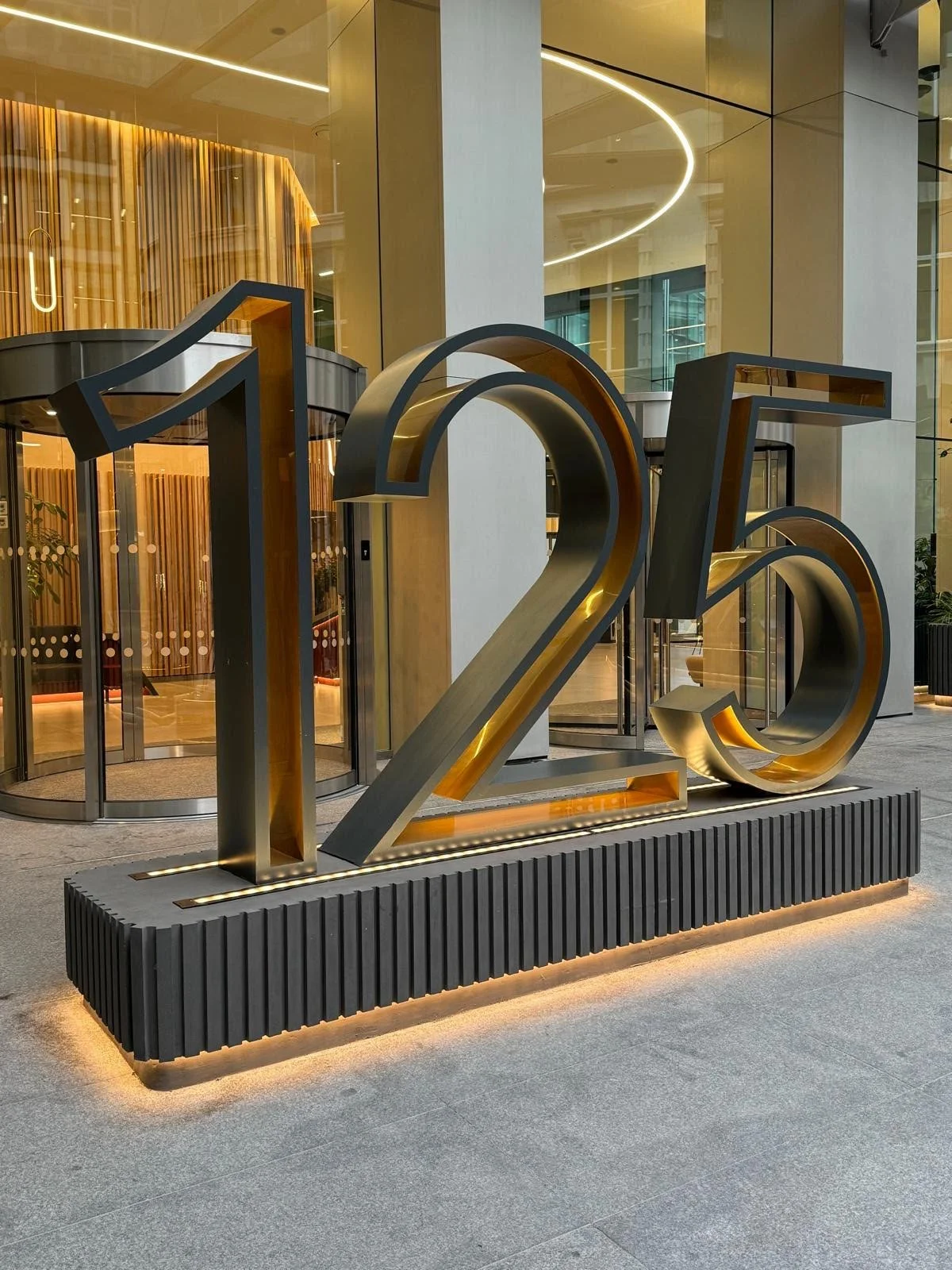 Bespoke halo-lit built-up metal signage featuring the numbers 125 with warm white LED backlighting against a dark architectural wall.