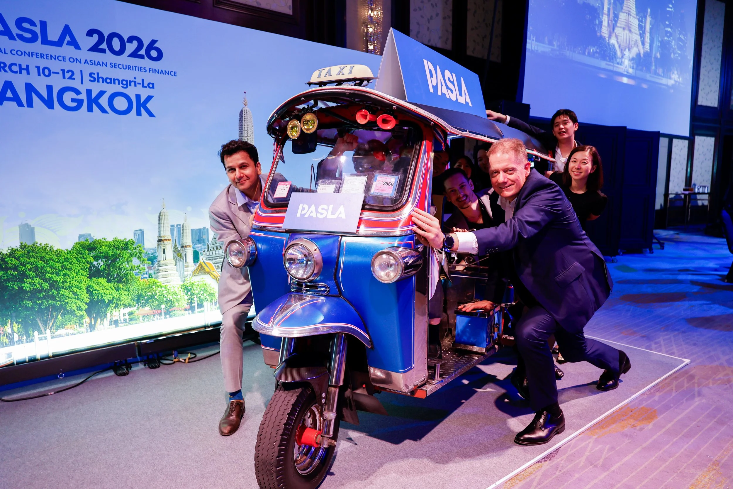 Group of people around a three-wheeled tuk-tuk vehicle on a stage at the PASLA 2026 conference in Bangkok, March 10-12, 2026.
