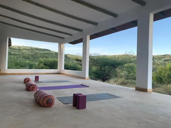 Yoga mats, bolsters, and blocks arranged on a covered outdoor patio with a view of scenic hills and trees.