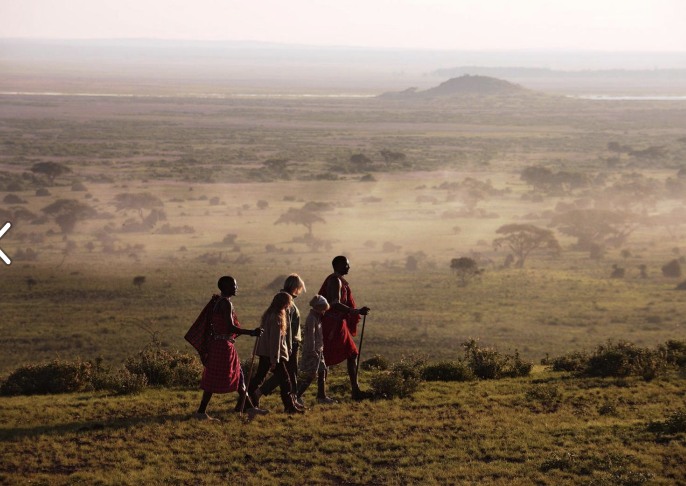 Group of five people walking across a grassy plain with a vast landscape and distant trees in the background