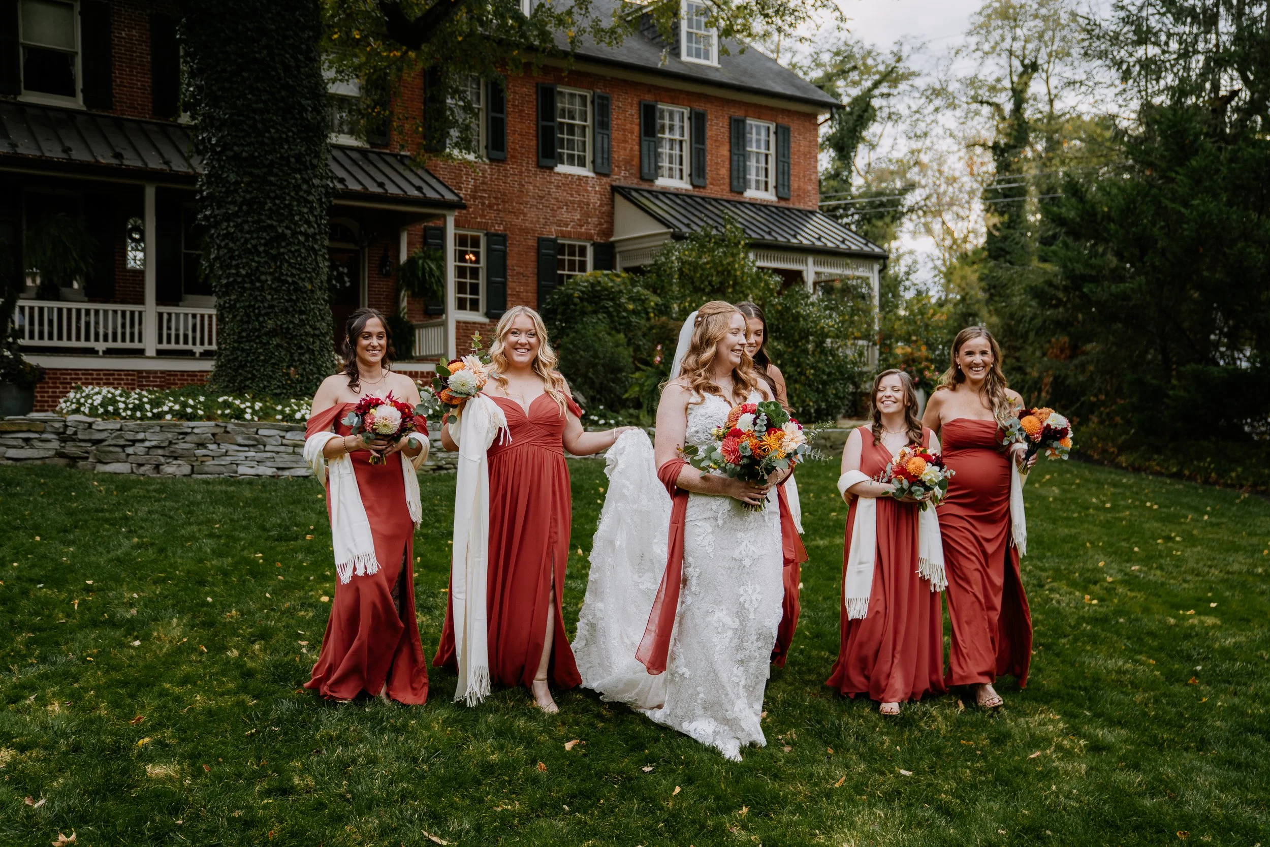 bride and bridesmaids are walking together and laughing on a front lawn of the brick house at Stone Mill Inn