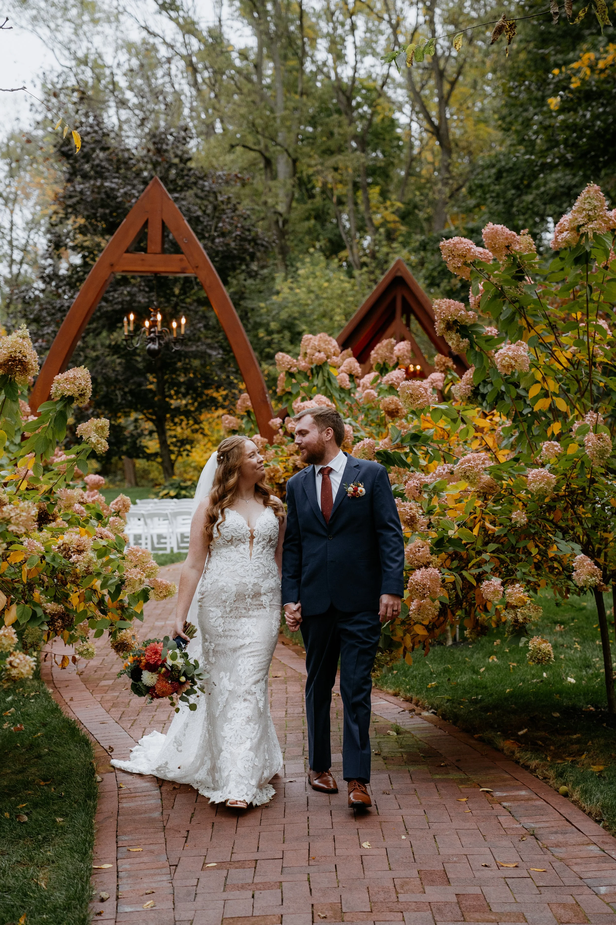 Bride and groom holding hands beneath hydrangeas at the Abbey at Stone Mill Inn in Hallam, PA