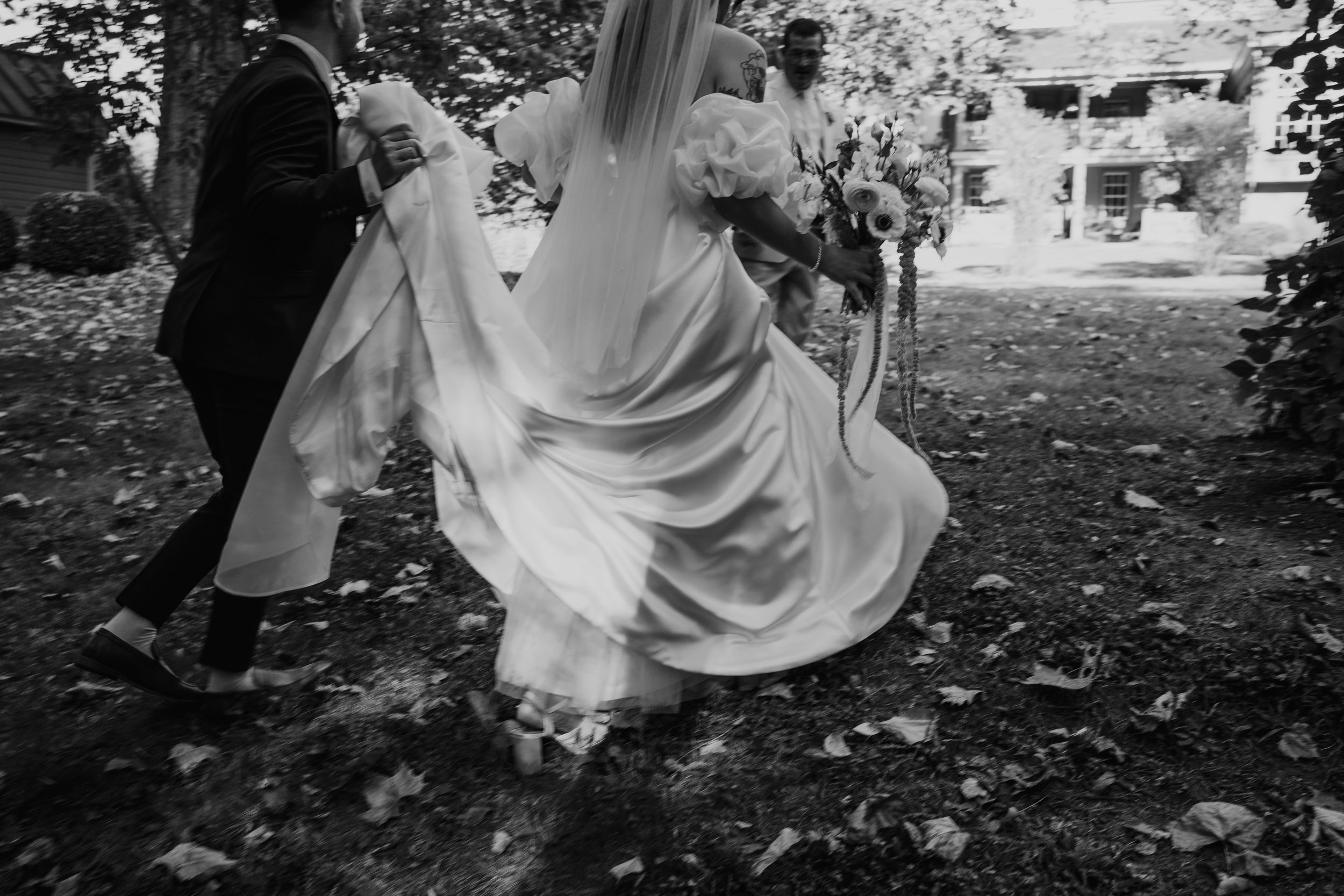 groom holding brides train as they walk together on their wedding day