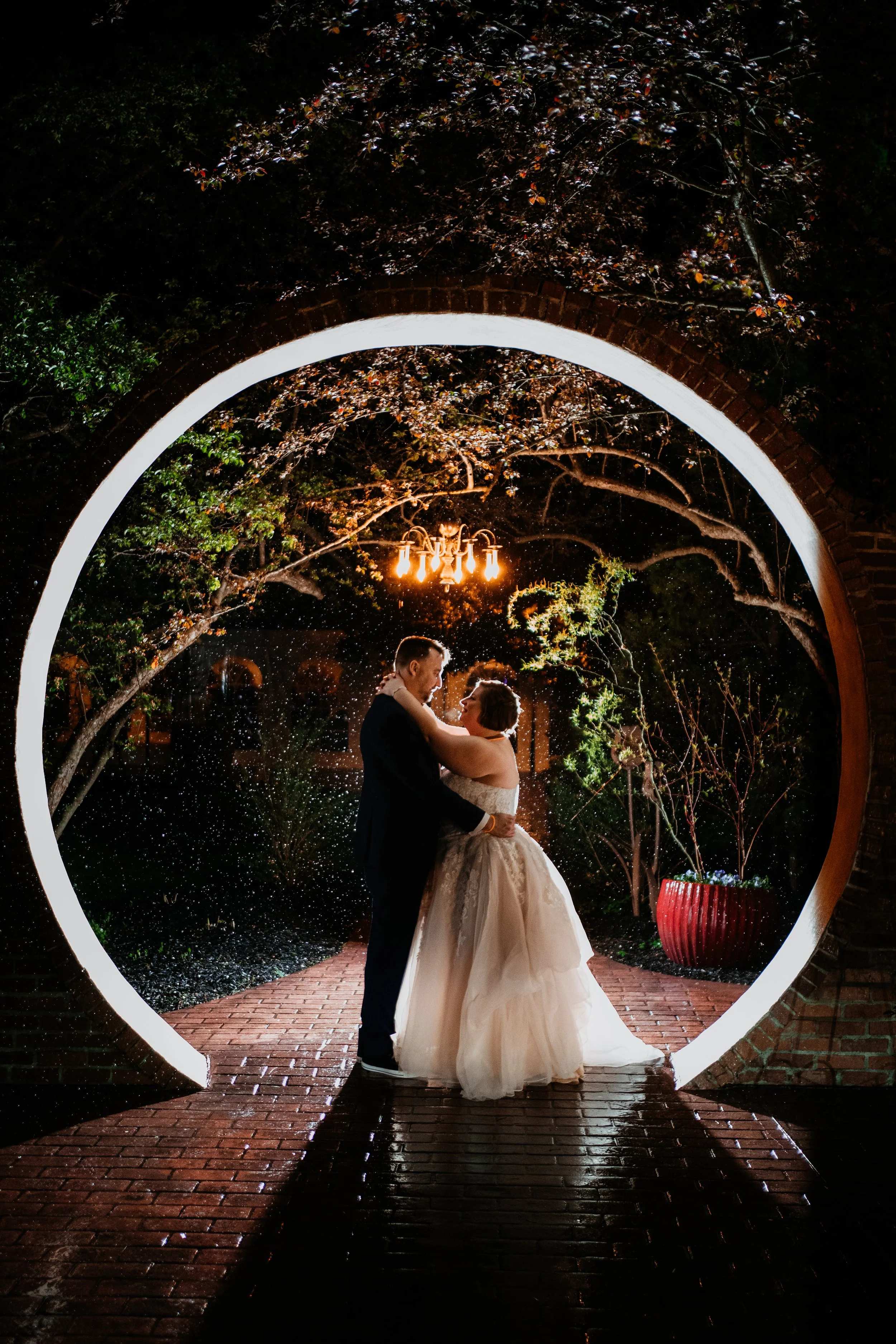 bride and groom embrace under a brick archway and chandelier at nighttime at the Stone Mill Inn
