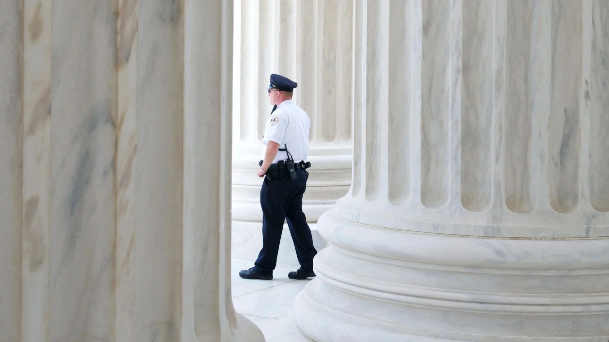 A police officer standing between large marble columns in a government building.