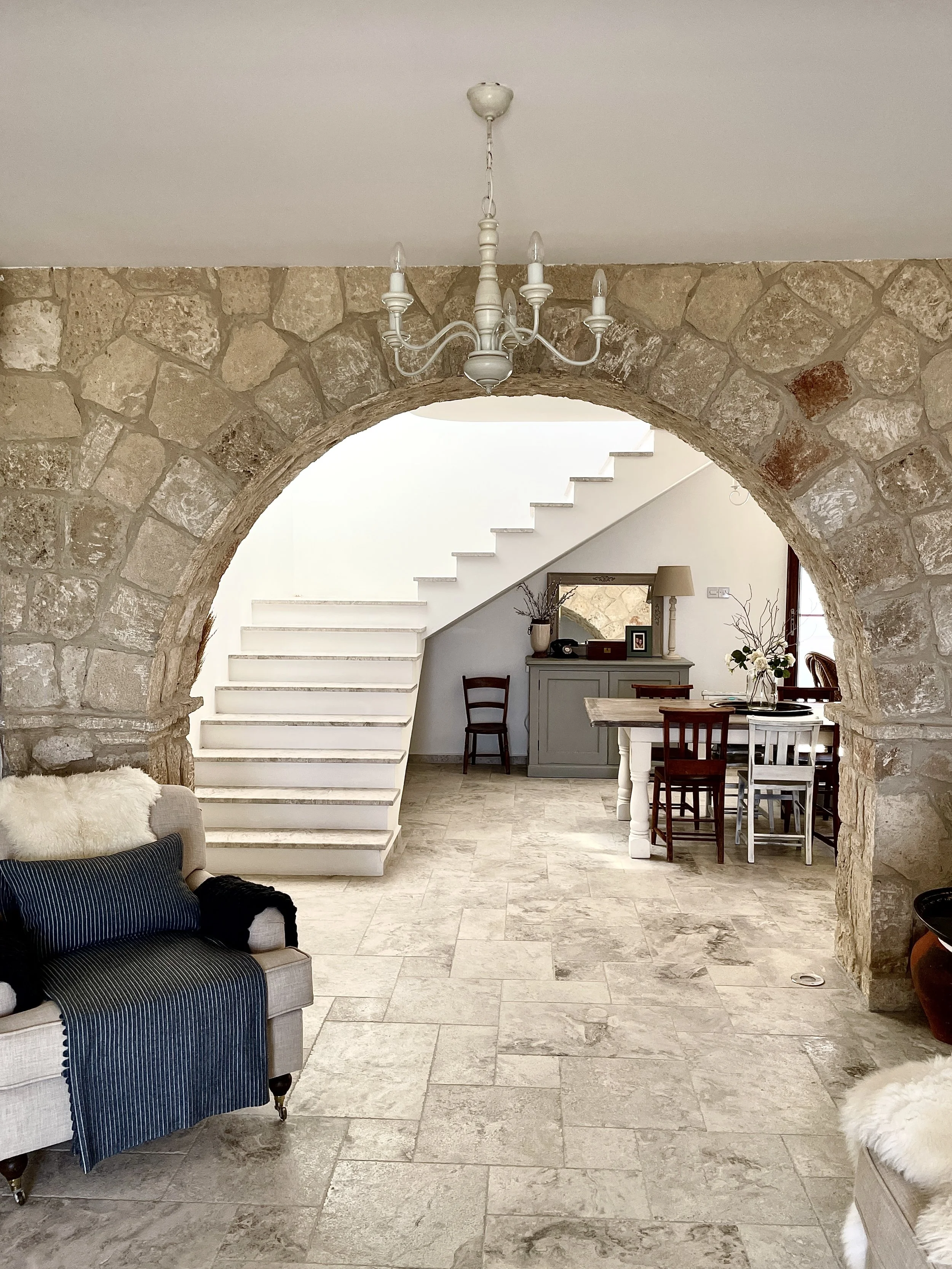 A living room with a stone archway, a staircase, and a dining area with a table and chairs.